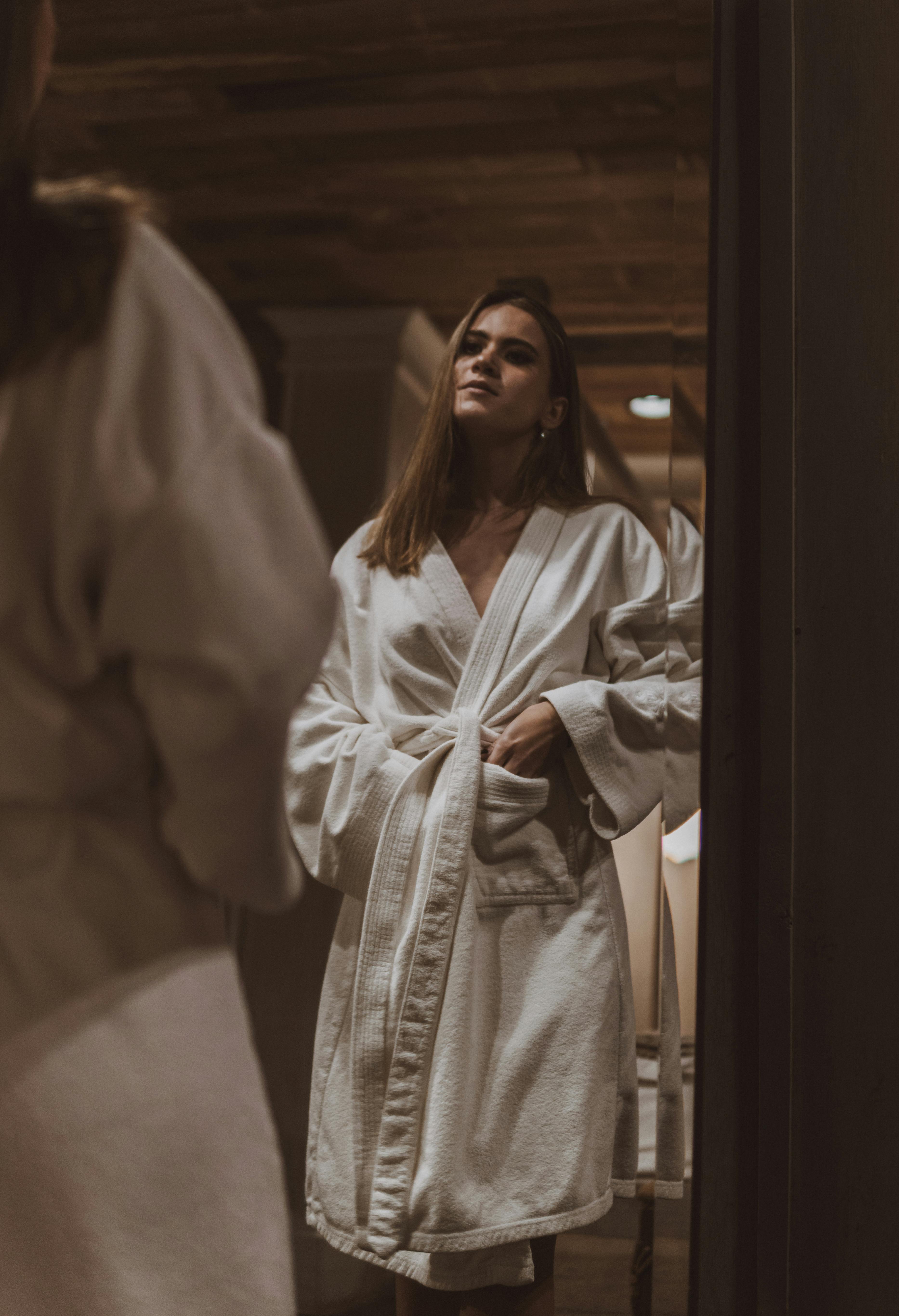 Eine Frau im Bademantel beim Blick in den Spiegel | Quelle: Pexels