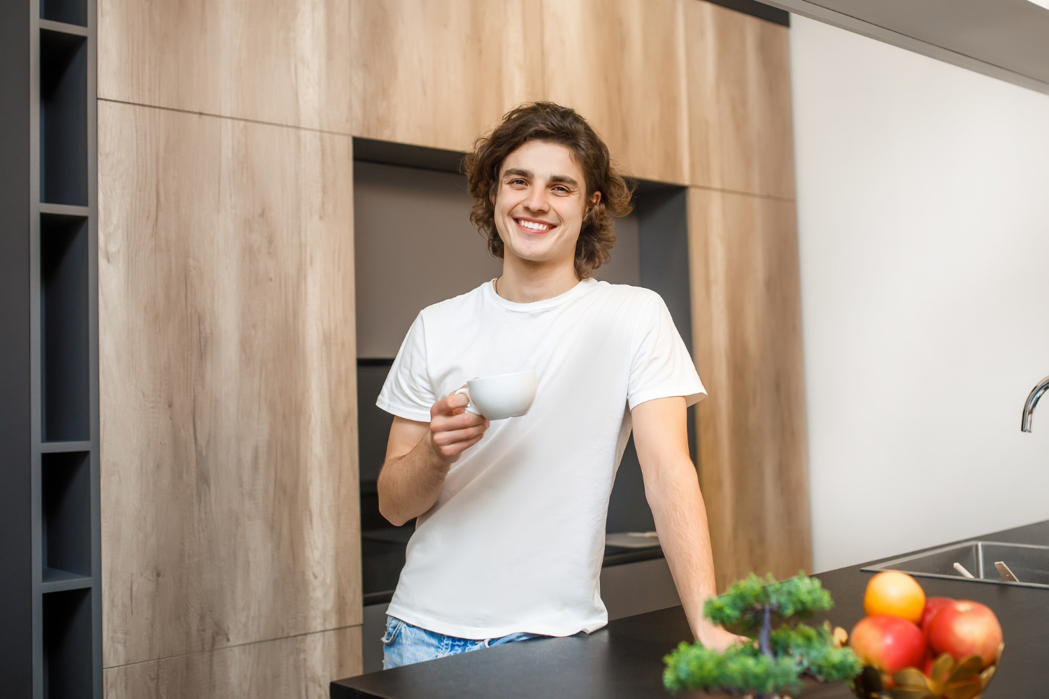 Ein lächelnder Mann, der eine weiße Keramiktasse hält und in der Küche steht | Quelle: Freepik