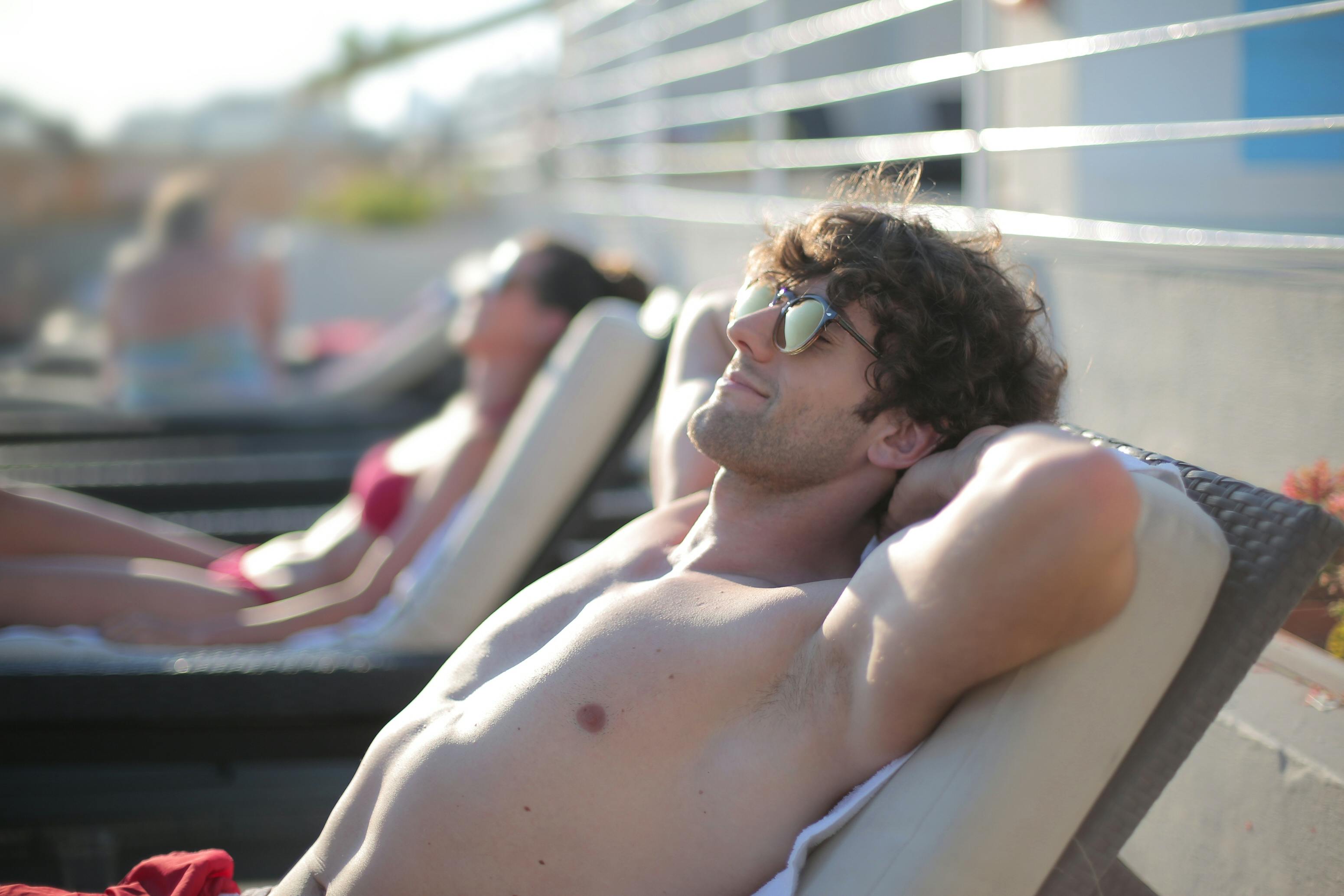 Ein glücklicher Mann trägt eine Sonnenbrille, während er auf einer Sonnenbank liegt | Quelle: Pexels