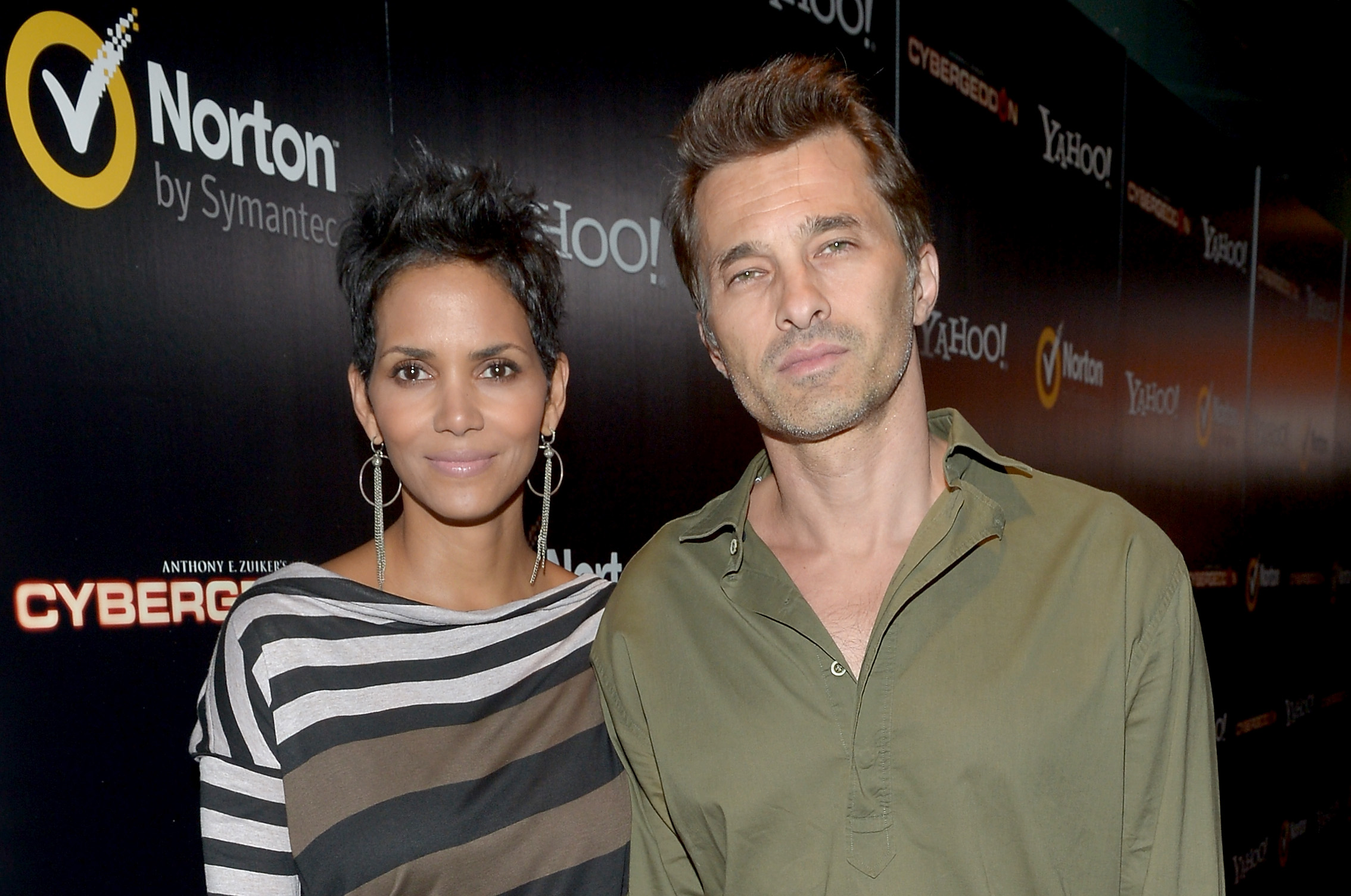 Die Schauspieler Halle Berry und Olivier Martinez standen bei der Premiere von „Cybergeddon“ am 24. September 2012 im Pacific Design Center in West Hollywood, Kalifornien, Seite an Seite auf dem schwarzen Teppich. Berry trug ein asymmetrisches Oberteil mit U-Boot-Ausschnitt und auffälligen Querstreifen, dazu baumelnde Fransen-Ohrringe und einen strukturierten, stacheligen Pixie-Cut, während Martinez es in einem olivgrünen Hemd mit offenem Kragen eher lässig hielt. | Quelle: Getty Images