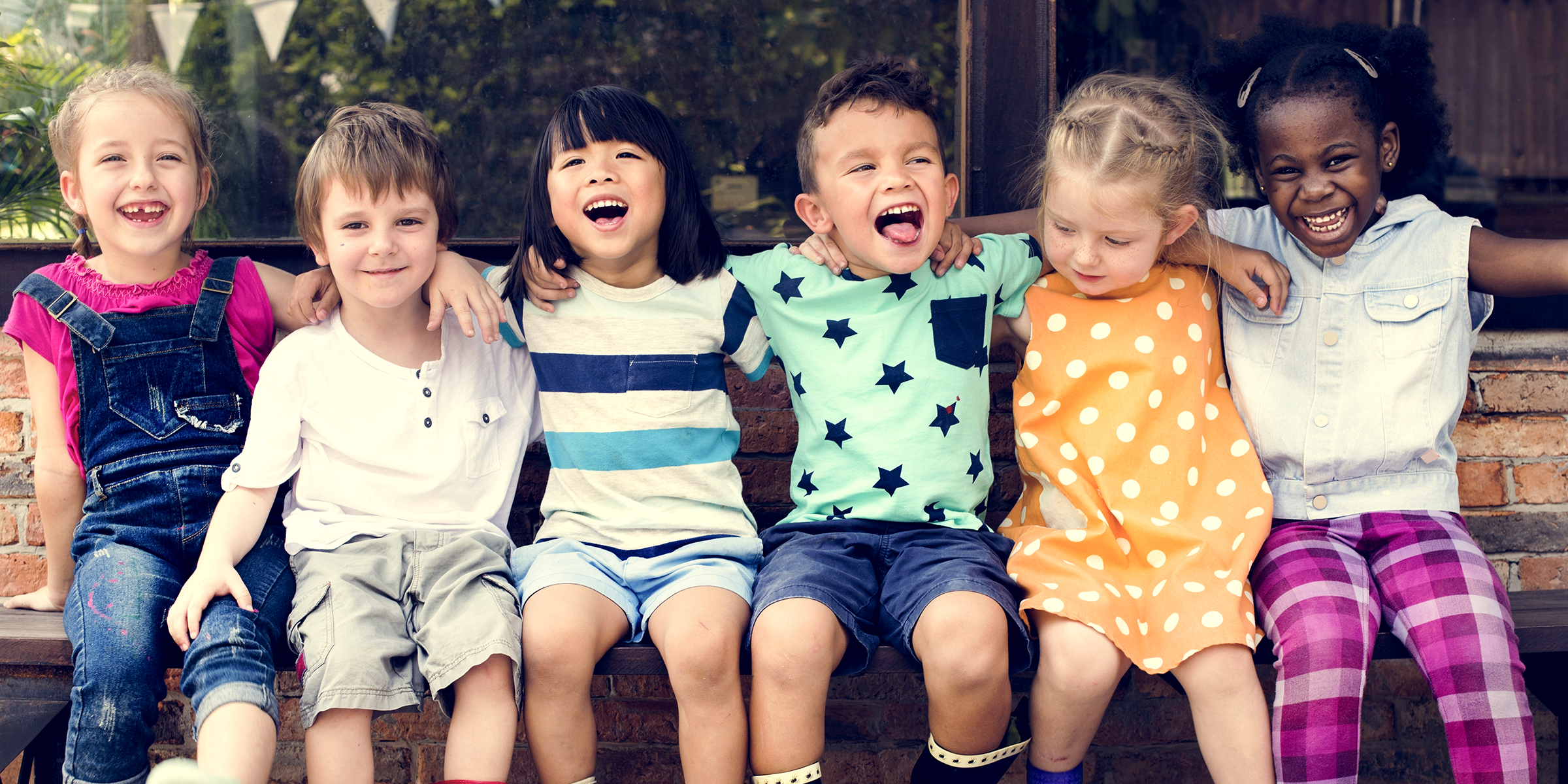 Fröhliche kleine Kinder, die auf einer Bank sitzen und lachen | Quelle: Shutterstock