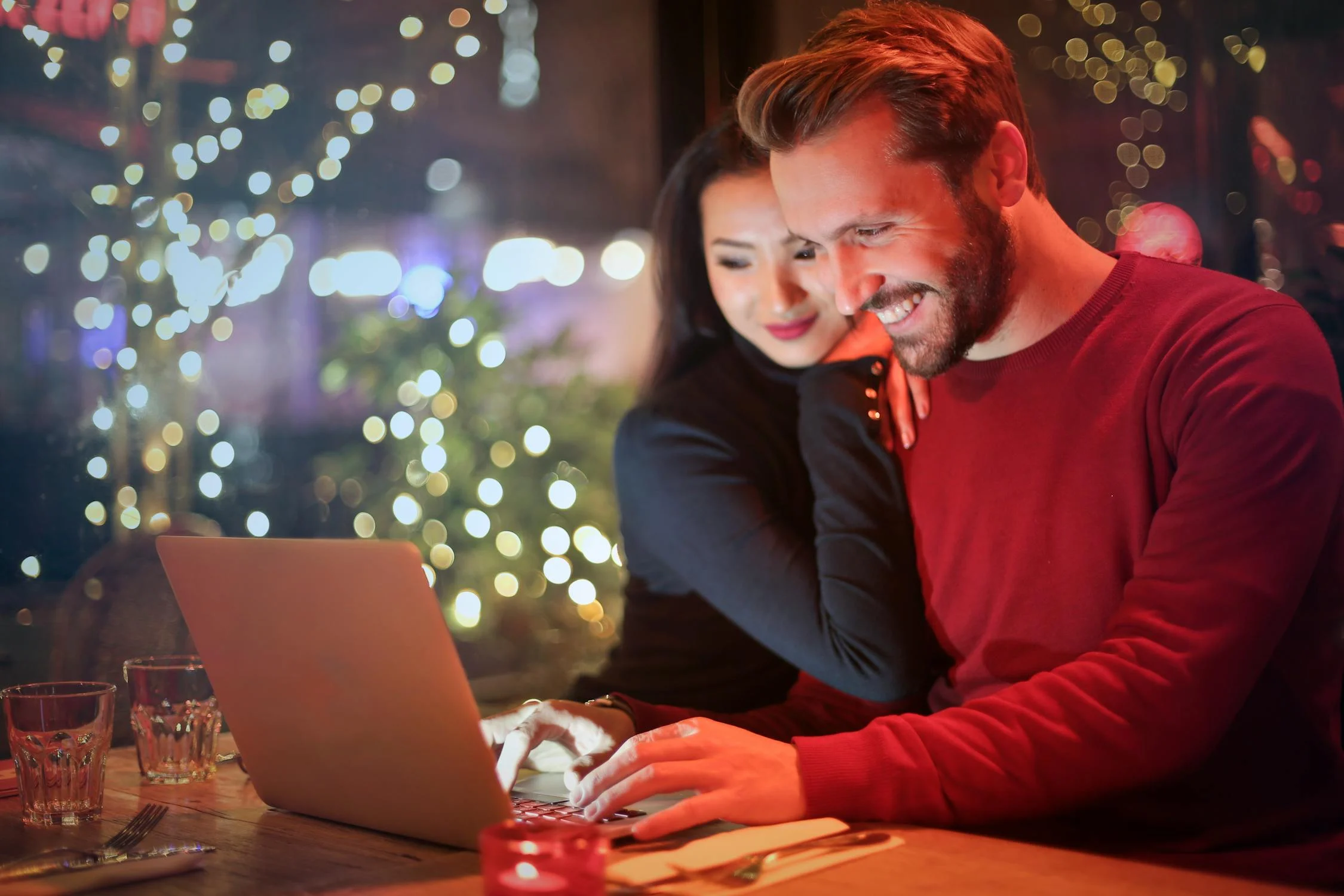 Eine Frau lehnt sich an einen Mann, der lächelnd an seinem Laptop arbeitet | Quelle: Pexels