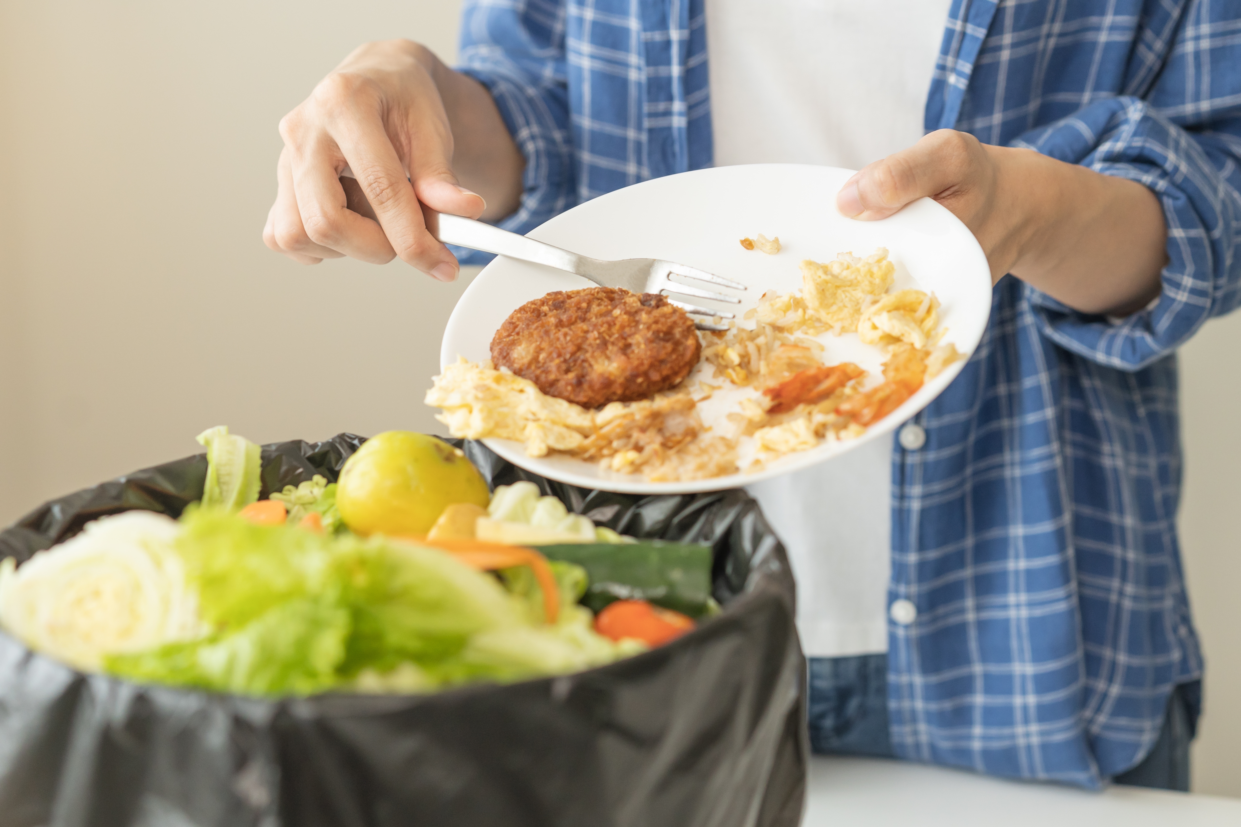 Ein Mann wirft Essen von einem Teller in den Mülleimer | Quelle: Shutterstock