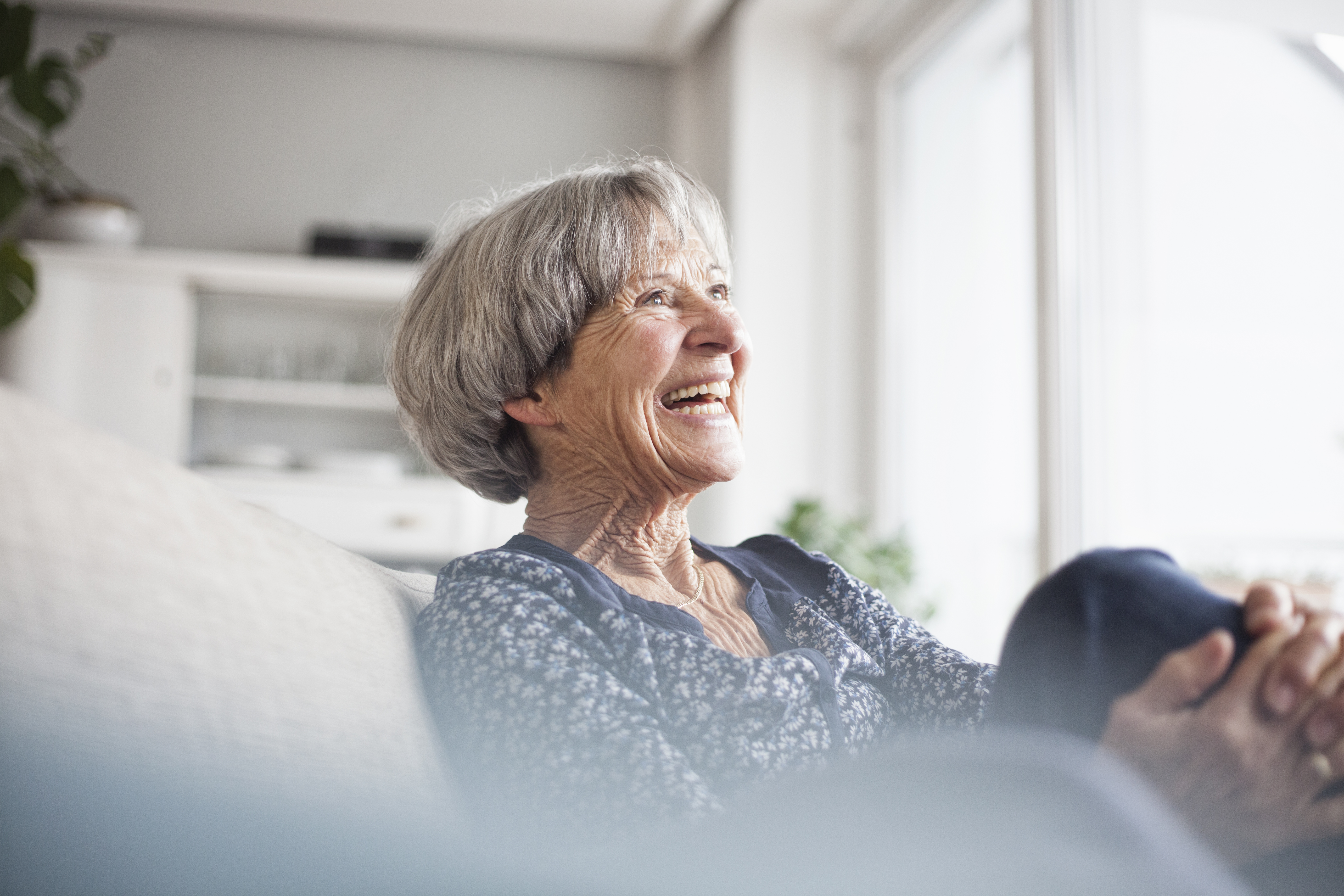 Porträt einer lachenden älteren Frau, die zu Hause auf der Couch sitzt | Quelle: Getty Images