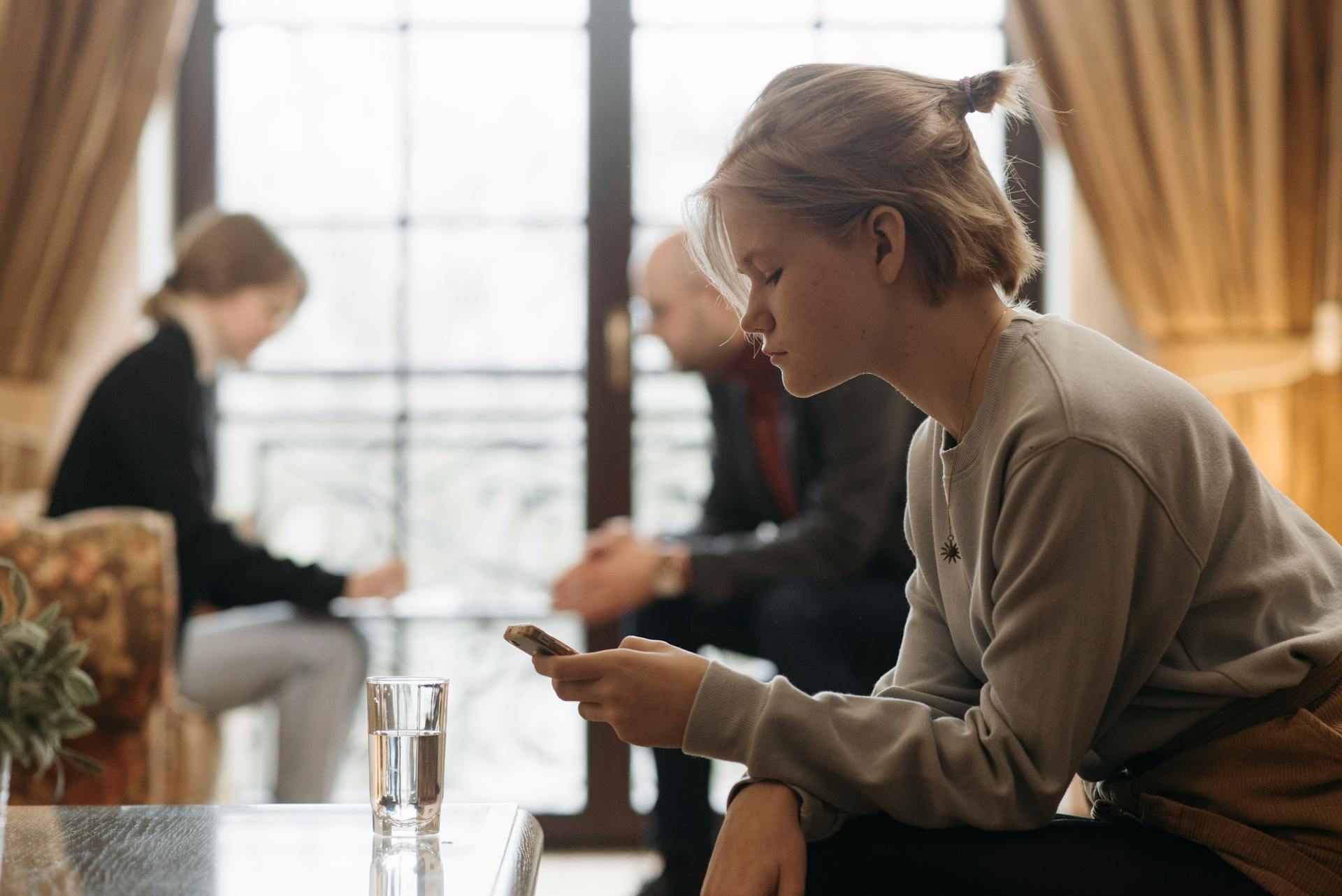 Ein ernstes Mädchen, das auf ihr Telefon schaut, während im Hintergrund andere Menschen erscheinen | Quelle: Pexels