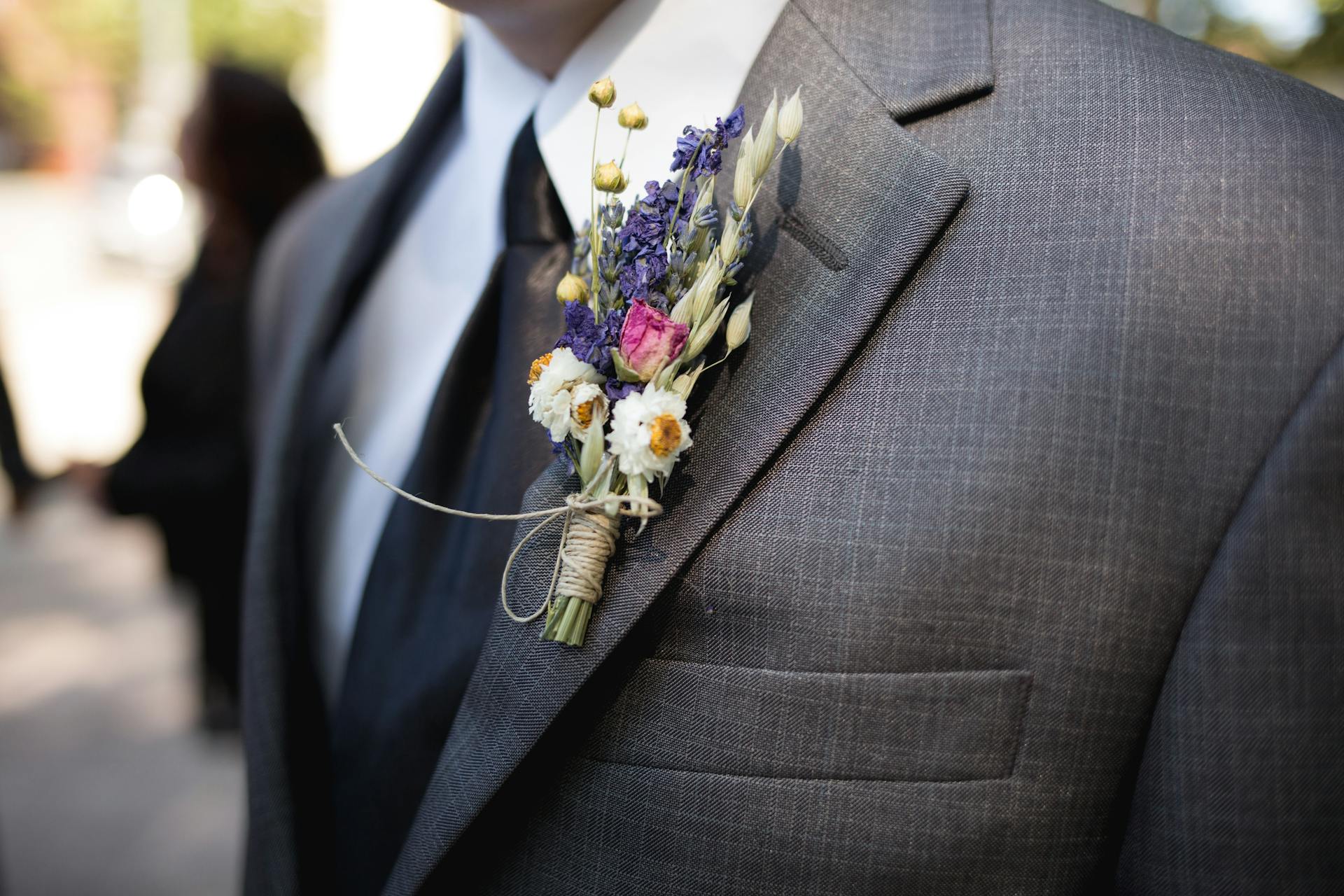 Eine Blumenboutonniere auf der grauen Anzugsjacke des Bräutigams | Quelle: Pexels