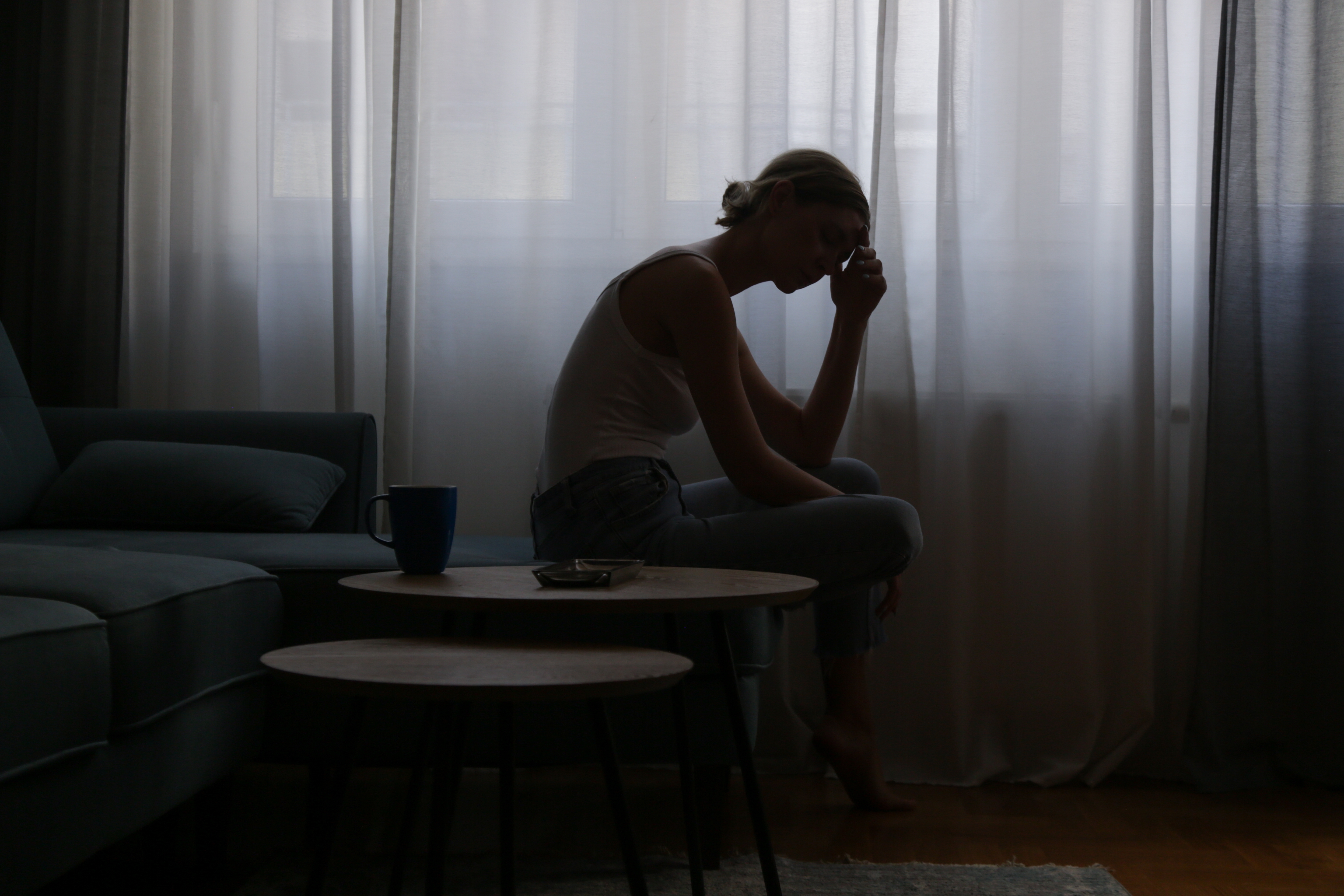 Depressive junge Frau, die auf einem Sofa neben einem Fenster sitzt | Quelle: Shutterstock
