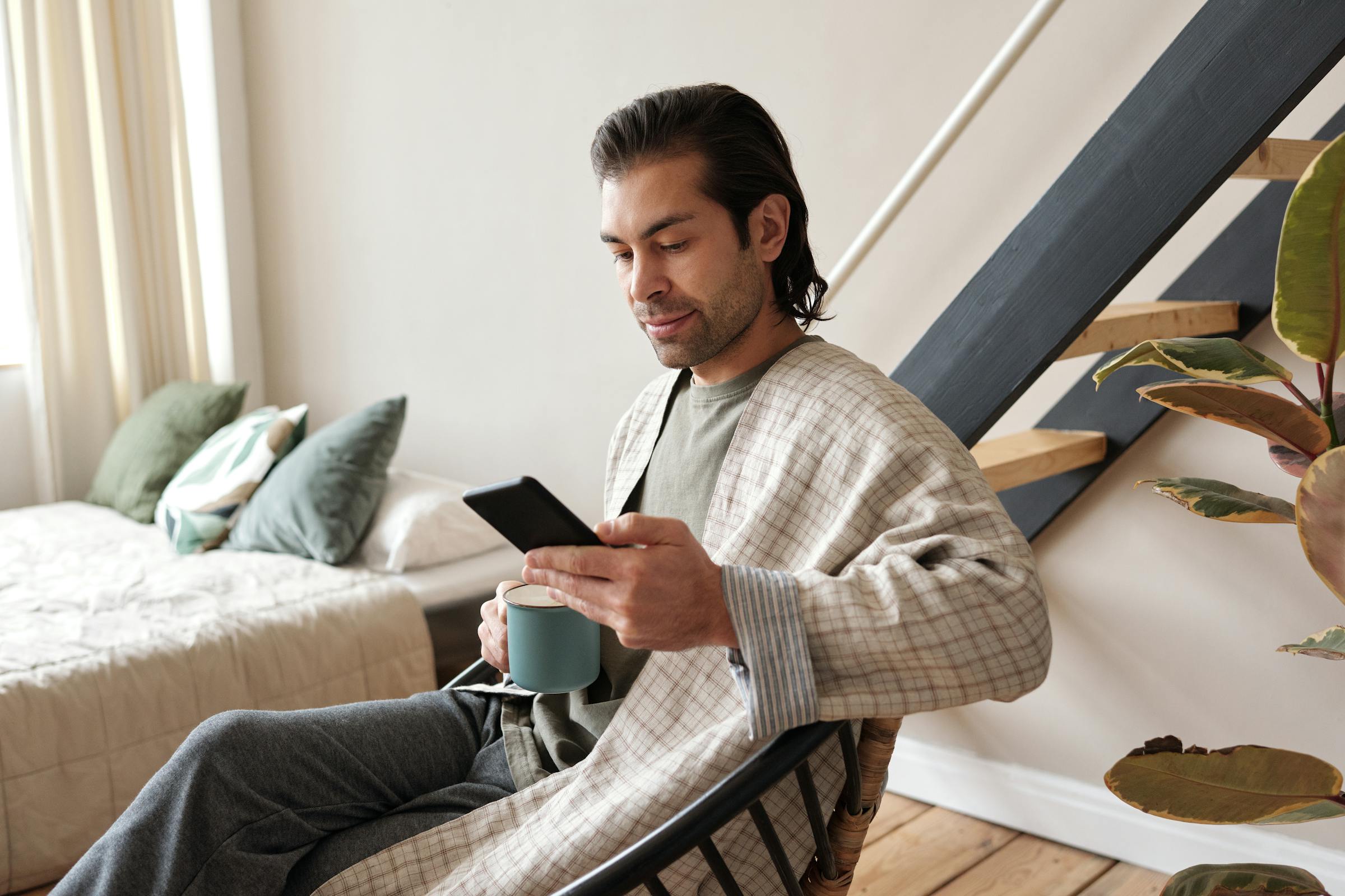 Mann schaut auf sein Handy, während er Kaffee trinkt | Quelle: Pexels