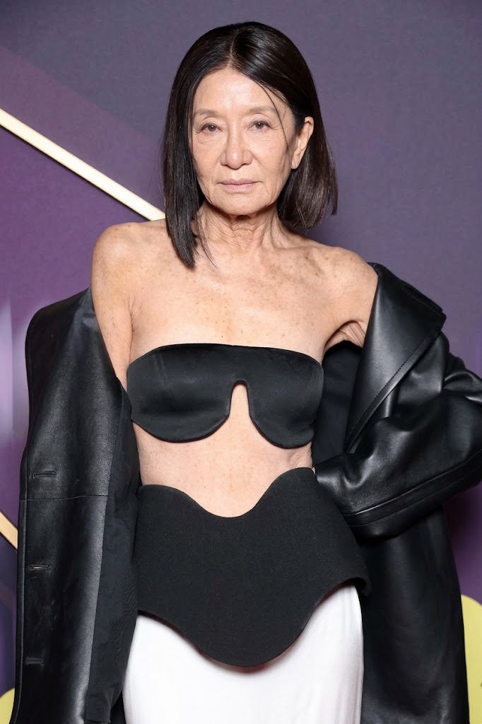 Dieses KI-generierte Bild zeigt Vera Wang, wie sie auf natürliche Weise altert, und lässt dabei ihren auffälligen Look vom roten Teppich der EE BAFTA Film Awards 2025 in London wieder aufleben. Das digitale Konzept zeigt die Designerin mit einem schicken, kurz geschnittenen Bob, authentischen feinen Fältchen und sonnengeküsster, reifer Haut. Sie trägt das vielbeachtete, skulpturale schwarze Bandeau-Top, dazu einen passgenauen, geschwungenen Peplum-Taillenbereich, eine drapierte schwarze Lederjacke und einen weißen, bodenlangen Rock. | Quelle: Gemini