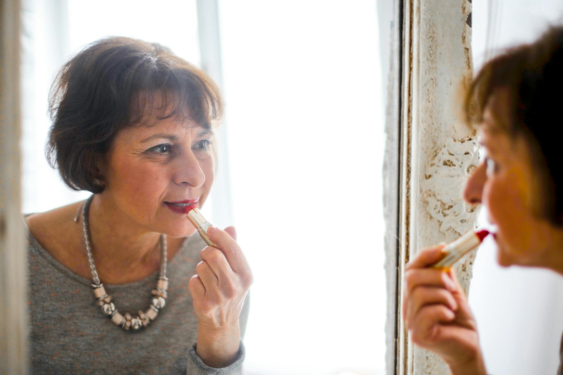 Eine ältere Frau trägt vor dem Spiegel Lippenstift auf | Quelle: Pexels