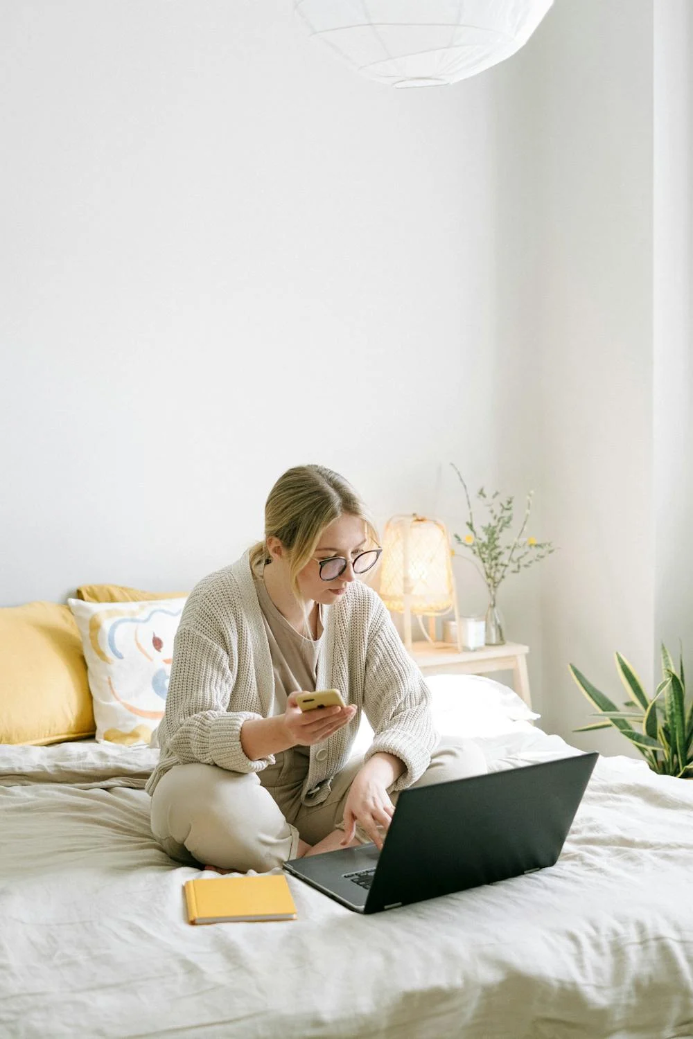 Eine Frau, die mit ihrem Telefon in der Hand auf ihren Laptop schaut | Quelle: Pexels