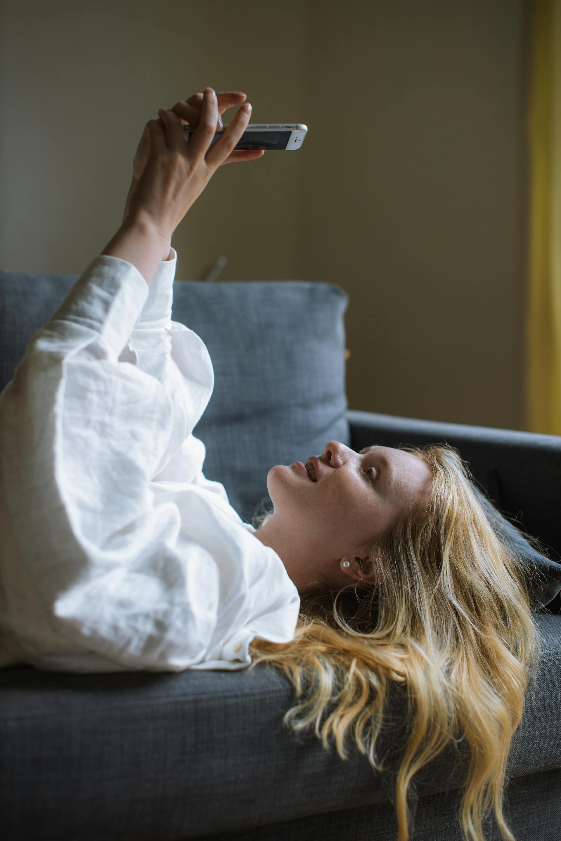 Eine junge Frau benutzt ihr Telefon, während sie auf einem Sofa liegt | Quelle: Pexels