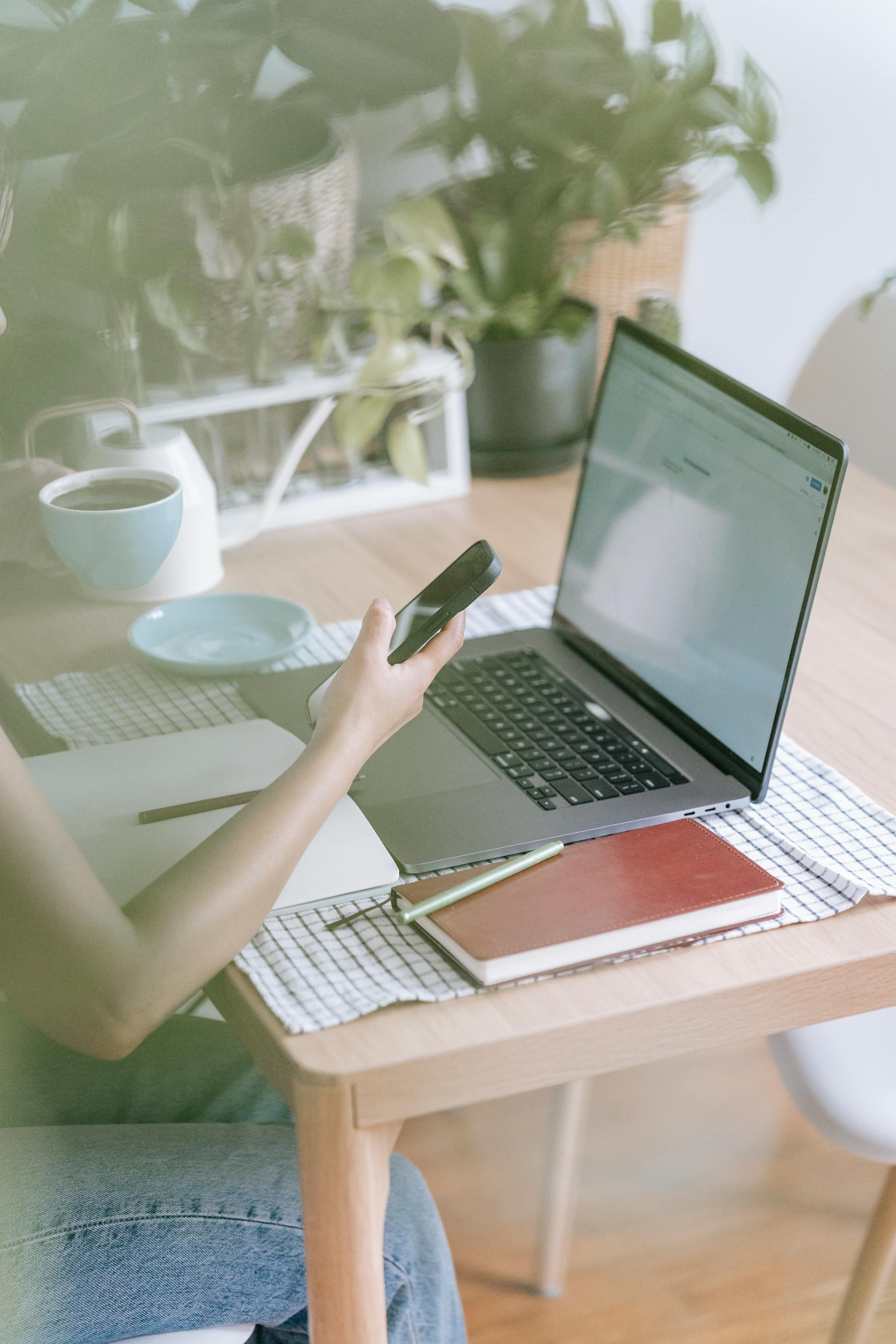 Eine Nahaufnahme einer Frau, die ihr Telefon in der Hand hält, während sie an ihrem Laptop arbeitet | Quelle: Pexels