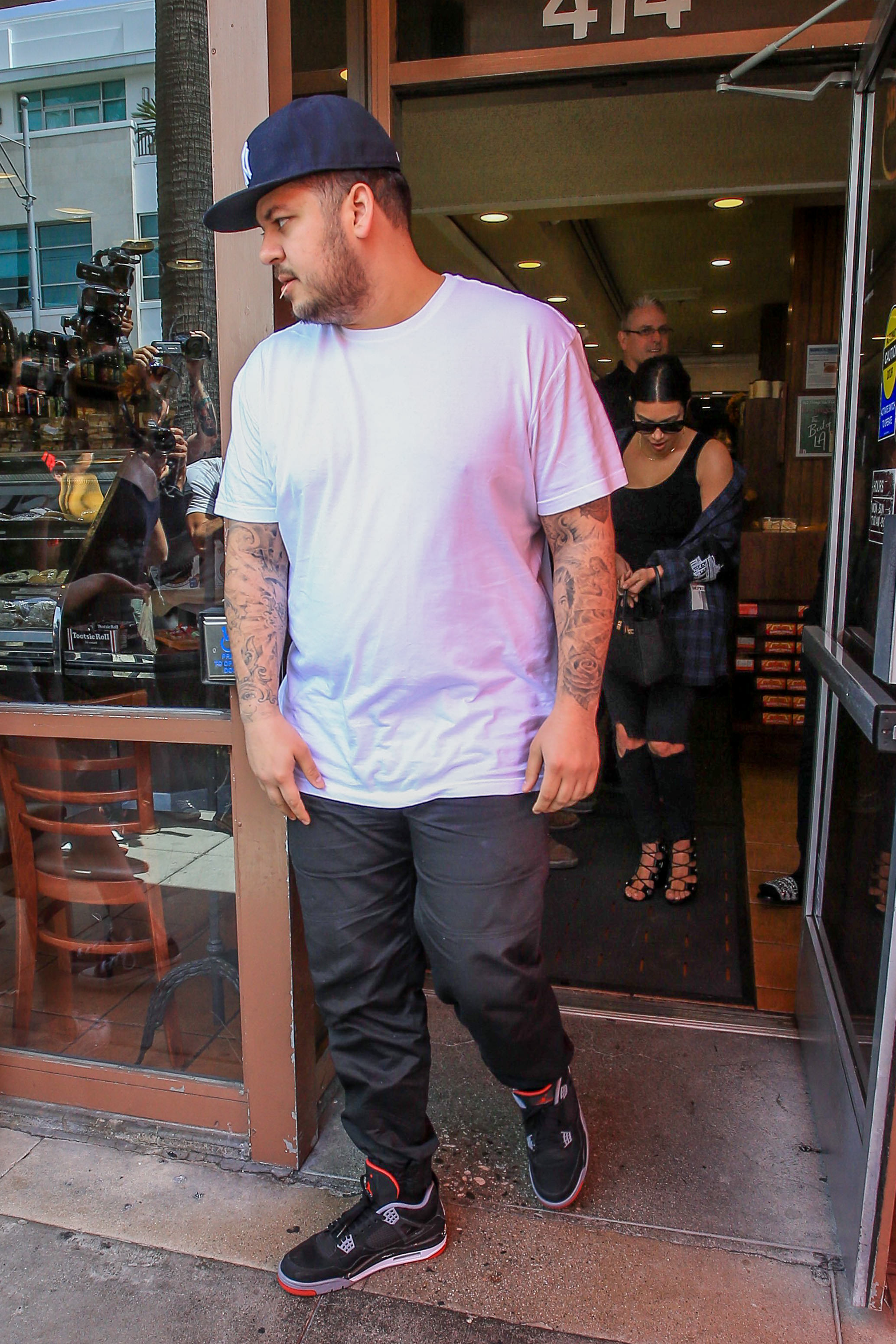Rob Kardashian verlässt ein Restaurant in Los Angeles in einem weißen T-Shirt und einer Baseballkappe, während Kim Kardashian ihm folgt. Das Foto zeigt einen seltenen gemeinsamen öffentlichen Auftritt mit seiner Schwester in einer Zeit, in der er sich allmählich wieder wohler dabei fühlte, in der Öffentlichkeit zu erscheinen. | Quelle: Getty Images.