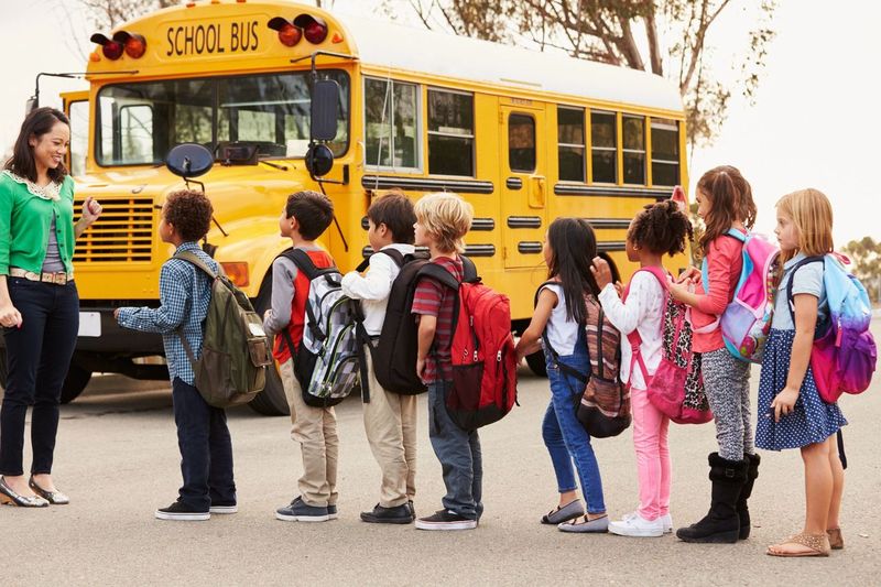 Schüler/innen, die vor einem Schulbus anstehen | Quelle: Shutterstock