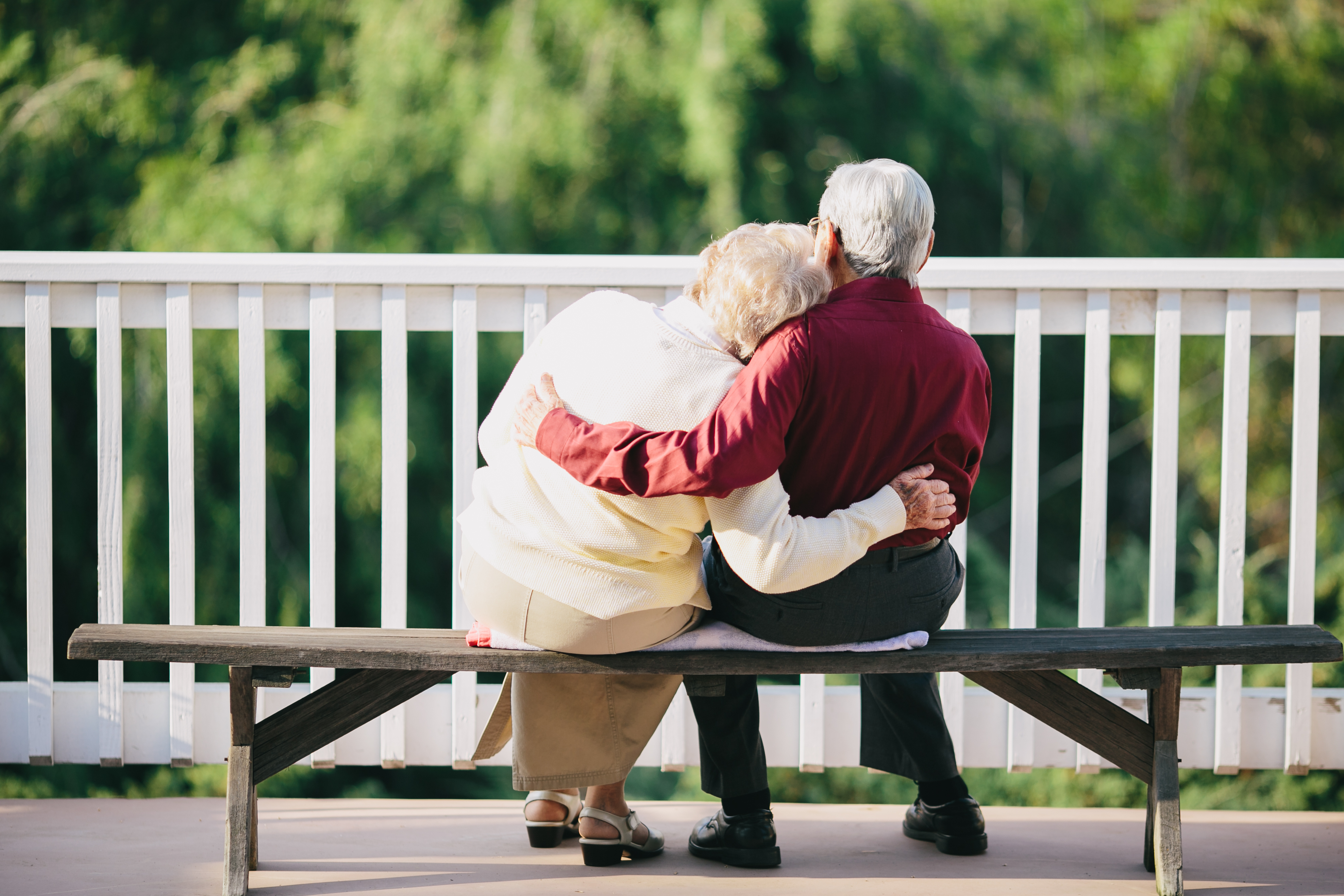 Ein älteres Paar, das sich umarmt, während es draußen auf einer Bank sitzt | Quelle: Shutterstock