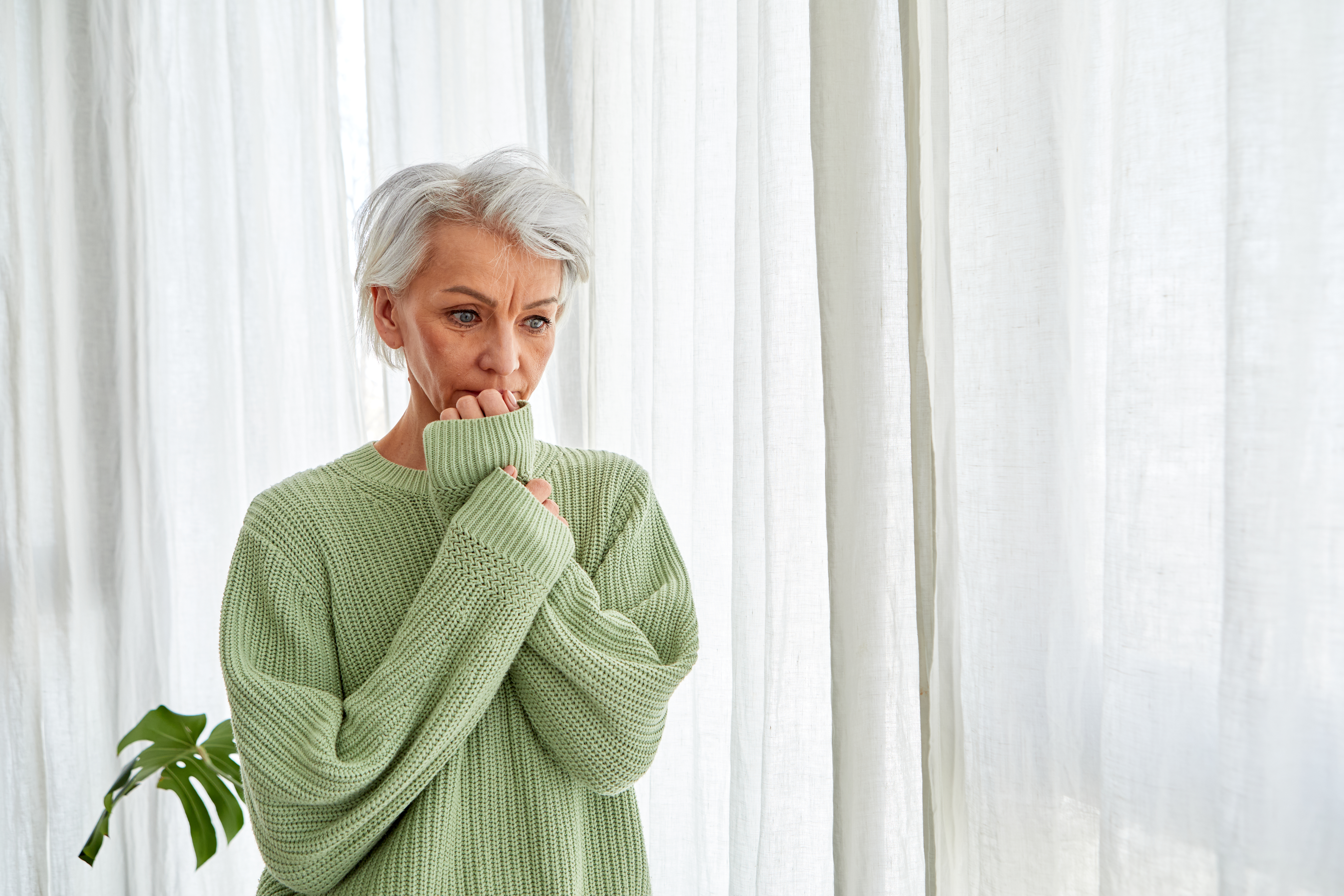 Frau mit grauem Haar kaut nervös an ihren Nägeln am Fenster | Quelle: Getty Images