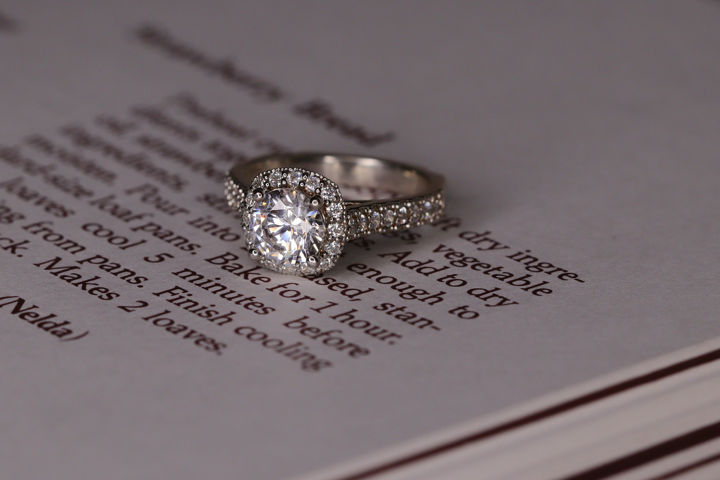 Ein Diamant-Verlobungsring aus Weißgold im Halo-Stil auf einem Buch | Quelle: Unsplash