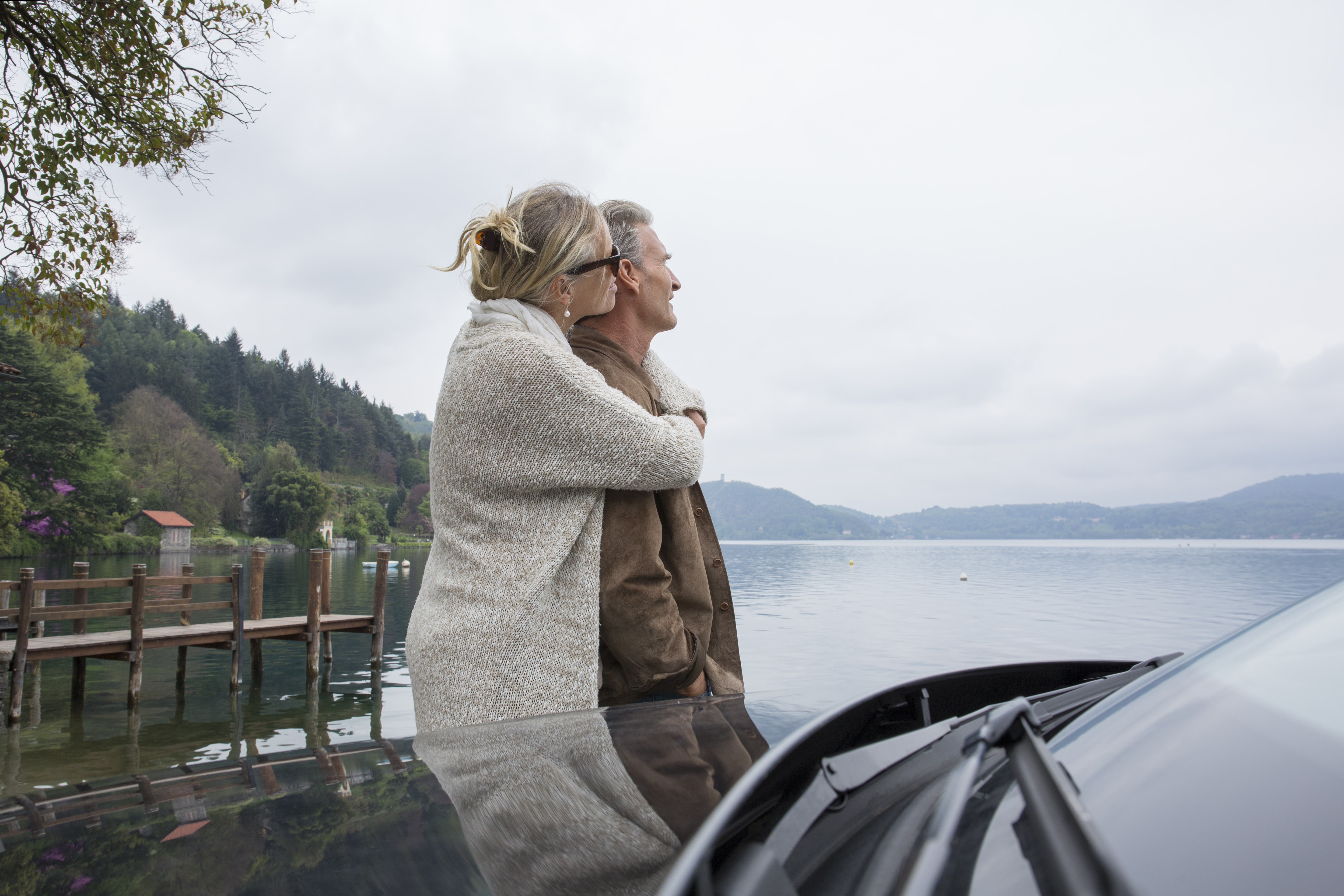Ein sich umarmendes Paar steht neben seinem Auto in der Nähe eines Sees | Quelle: Getty Images