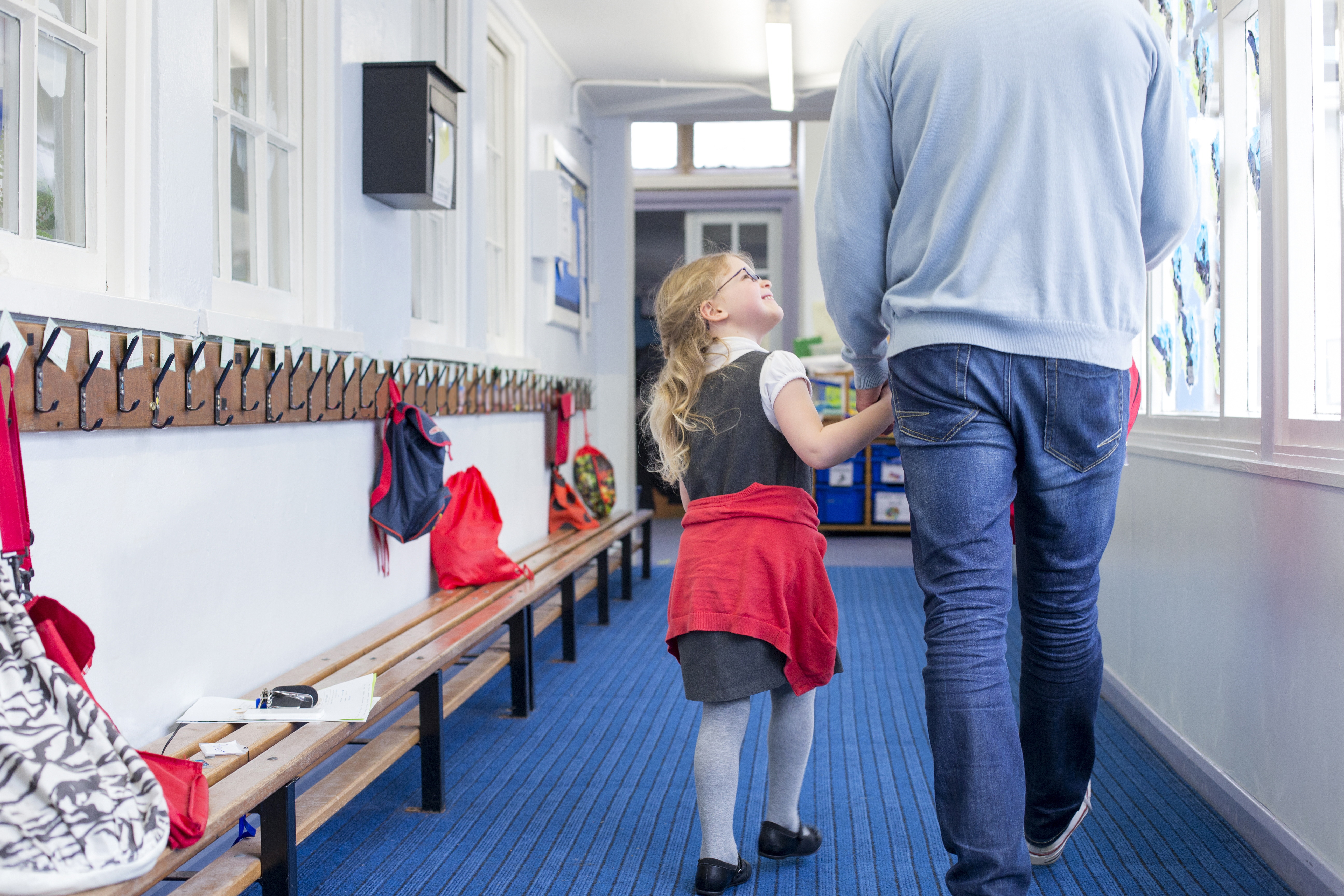 Kleines Mädchen, das lächelnd die Hand eines Mannes hält, während sie einen Korridor entlanggehen | Quelle: Shutterstock