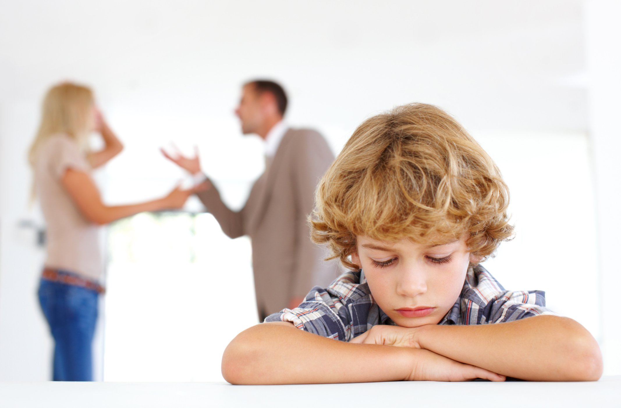 Ein trauriger Junge mit seinen Eltern, die sich im Hintergrund streiten | Quelle: Getty Images