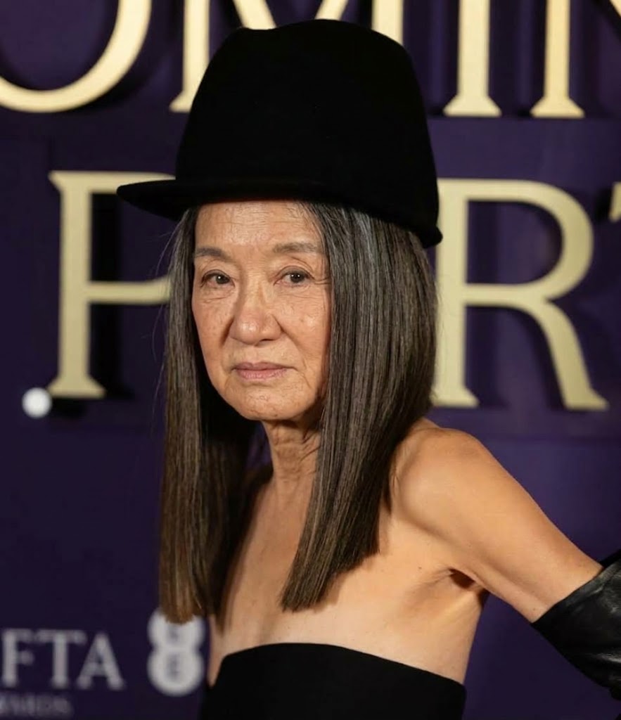 Inspiriert von ihrem Auftritt auf dem roten Teppich der BAFTA-Verleihung 2026 zeigt dieses KI-Konzept Vera Wang mit authentischen, reifen Gesichtskonturen, zarten Fältchen unter den Augen und silbergrauen, dunklen Haaren, die in einem geraden Schnitt fallen. Mit einem hohen schwarzen Cloche-Hut und einem trägerlosen schwarzen Ausschnitt, dazu passenden Leder-Opernhandschuhen vor einer violetten Fotowand, bietet die Darstellung einen realistischen Einblick, wie die Ikone auf natürliche Weise altert. | Quelle: Gemini