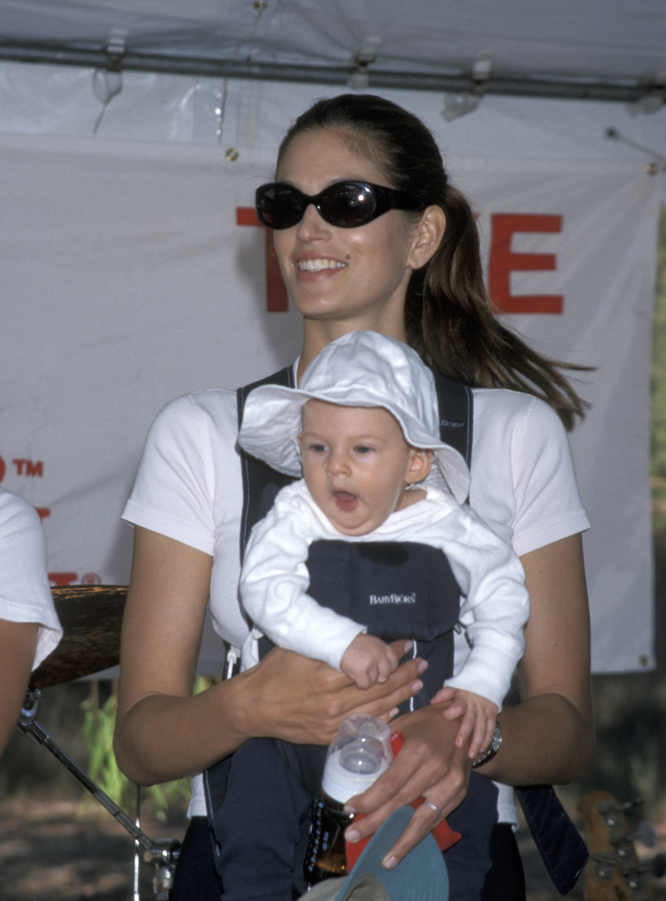 Cindy Crawford trägt den kleinen Presley Gerber bei der „Take a Hike“-Spendenveranstaltung in Malibu im Jahr 1999 und strahlt, während sie ihn fest in einer Fronttrage an sich drückt. Presley, der einen weißen Schlapphut und ein passendes Outfit trägt, gähnt leise, während er seine Flasche festhält – eine stille Erinnerung daran, wie winzig und engelsgleich er einst war, bevor er unter dem grellen Schein des Ruhms aufwuchs.