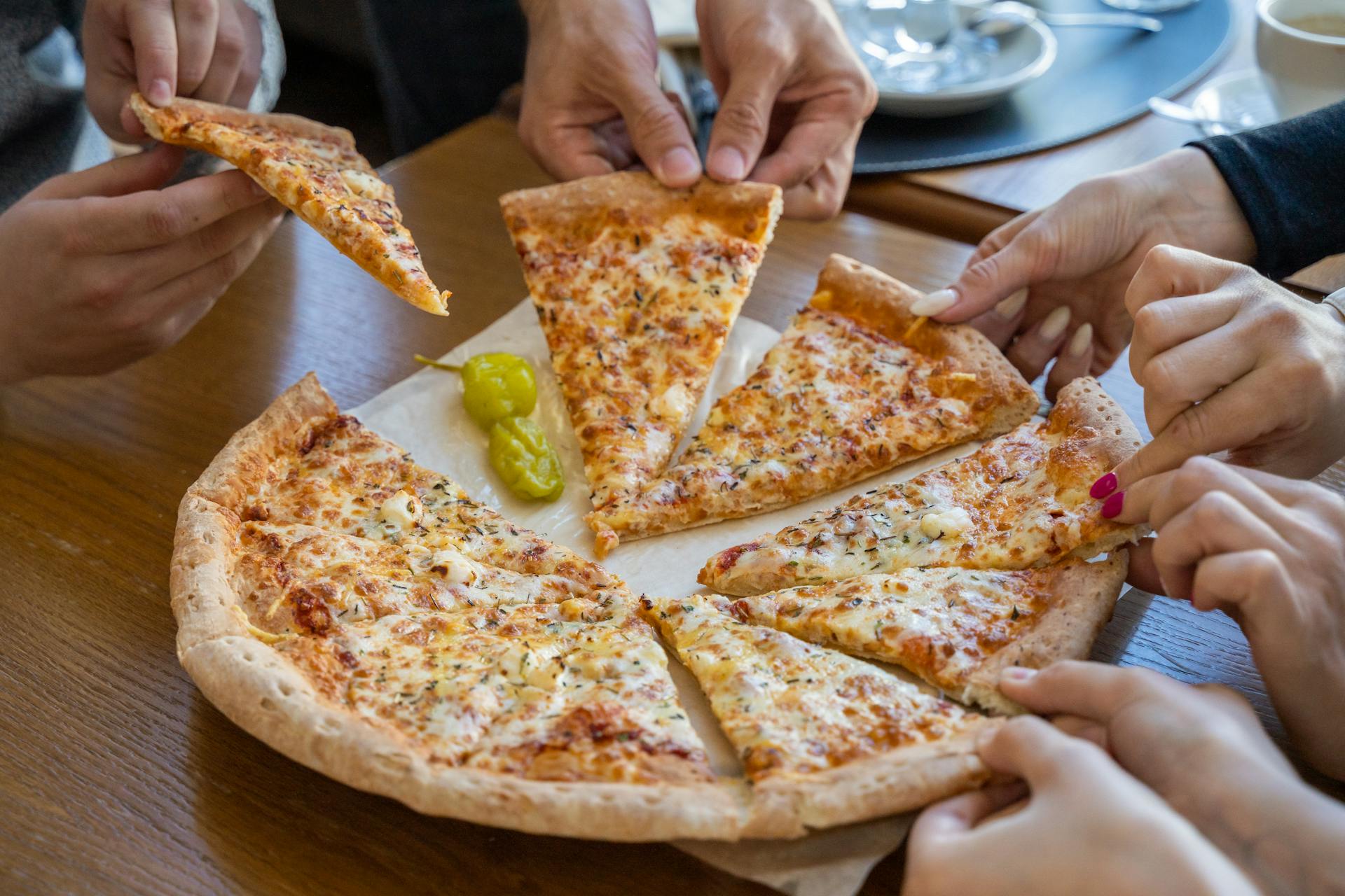 Menschen, die sich Scheiben von einer Pizza abschneiden | Quelle: Pexels