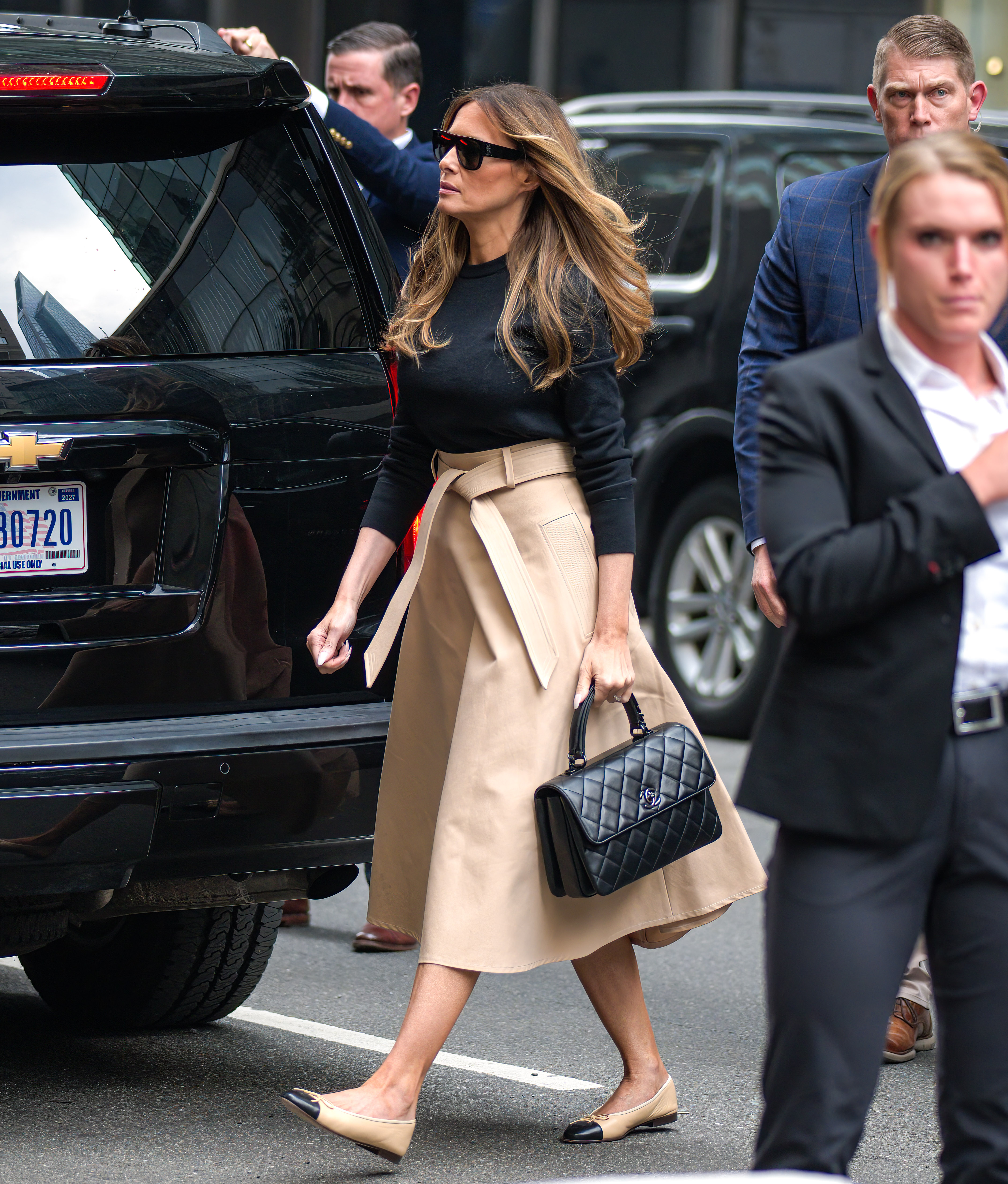 Melania Trump kommt am 8. Juni 2023 im Trump Tower in New York City an und trägt einen schwarzen Rundhals-Pullover, der in einen hoch taillierten, beigen Midirock mit Bindegürtel, dazu eine übergroße Sonnenbrille. Sie ergänzt das elegante Streetstyle-Outfit mit einer gesteppten Chanel-Handtasche und klassischen zweifarbigen, beige-schwarzen Ballerinas mit Zehenkappe.