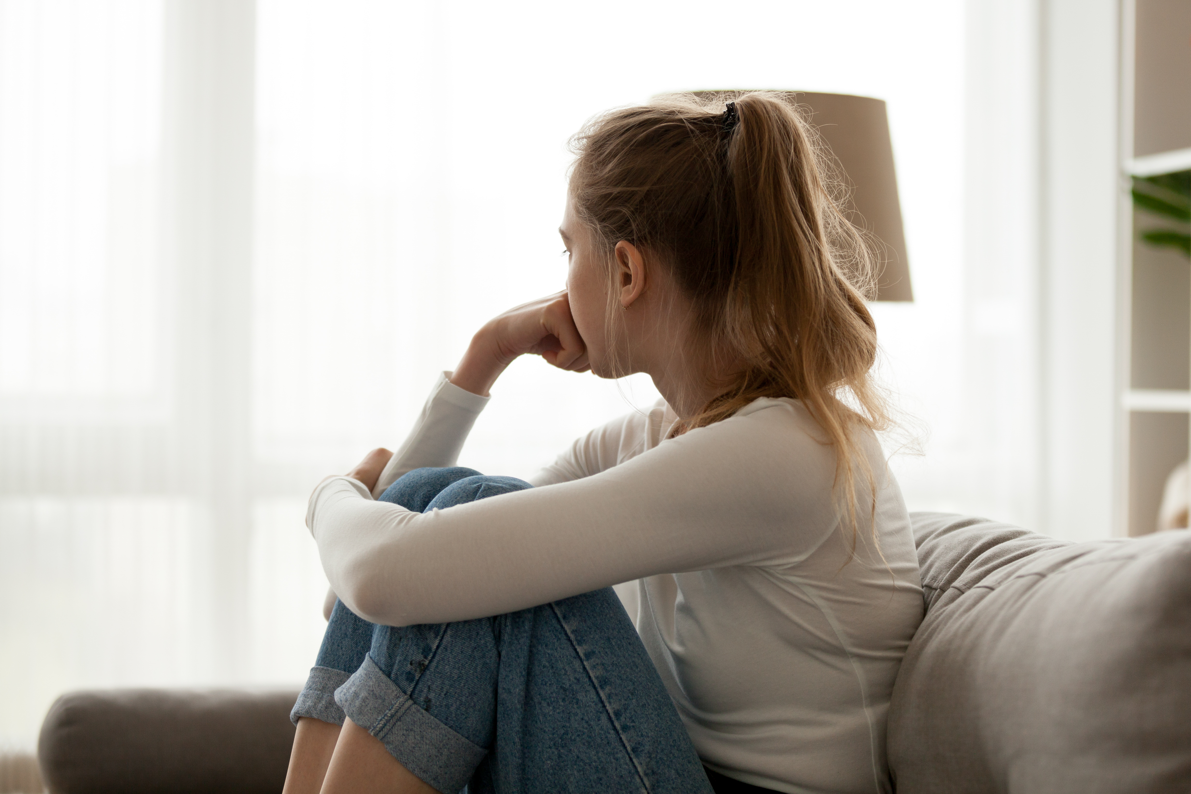 Ein Foto von einer Frau, die in Gedanken versunken auf einer Couch sitzt | Quelle: Shutterstock