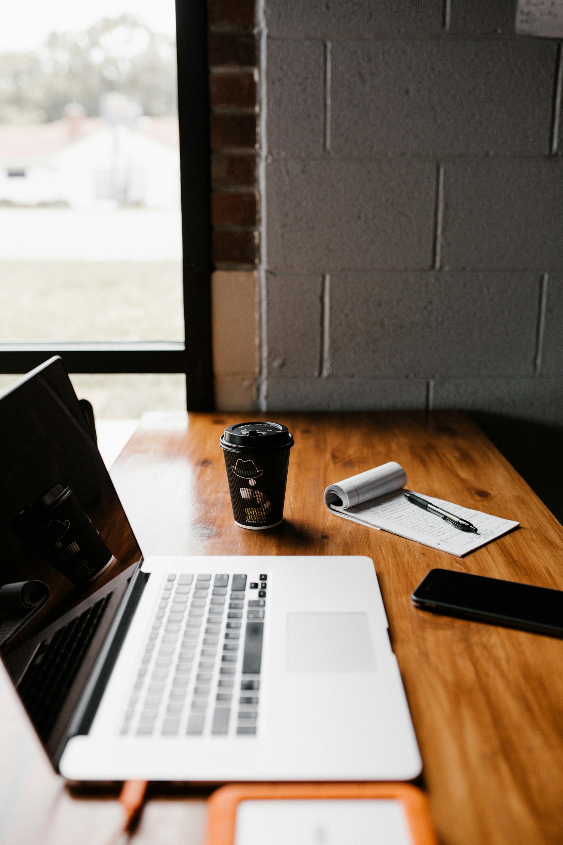 Eine Tasse Kaffee zum Mitnehmen neben einem Laptop auf einem Schreibtisch | Quelle: Pexels