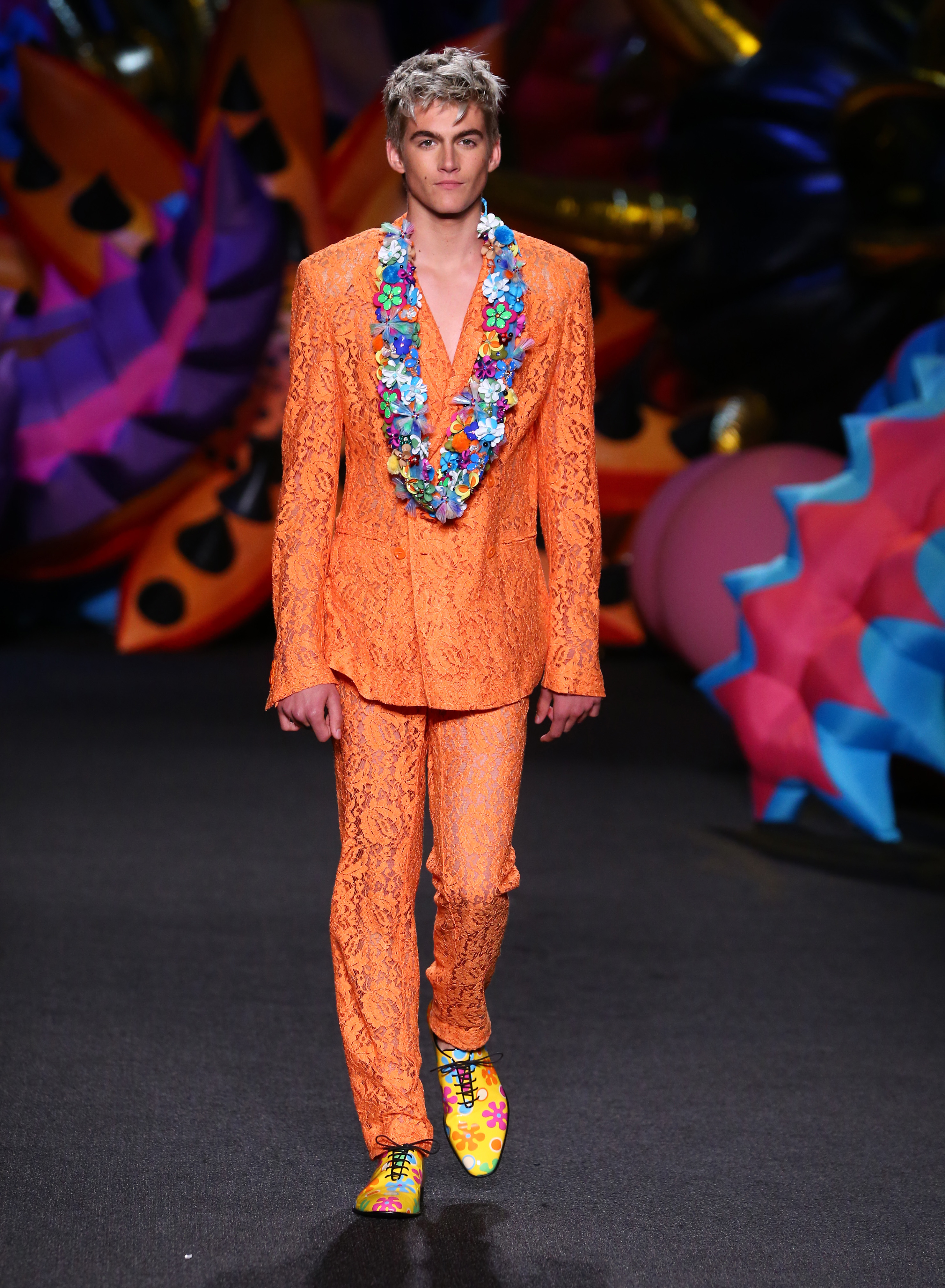 Presley Gerber bei seinem Model-Debüt auf dem Laufsteg der Moschino-Modenschau für Herren Frühjahr/Sommer 2017 und Damen Resort 2017 in Los Angeles, Kalifornien, am 10. Juni 2016. Er zog in einem leuchtend orangefarbenen Spitzenanzug, der durch eine bunte Blumen-Lei und gemusterte Anzugschuhe akzentuiert wurde, alle Blicke auf sich. | Quelle: Getty Images
