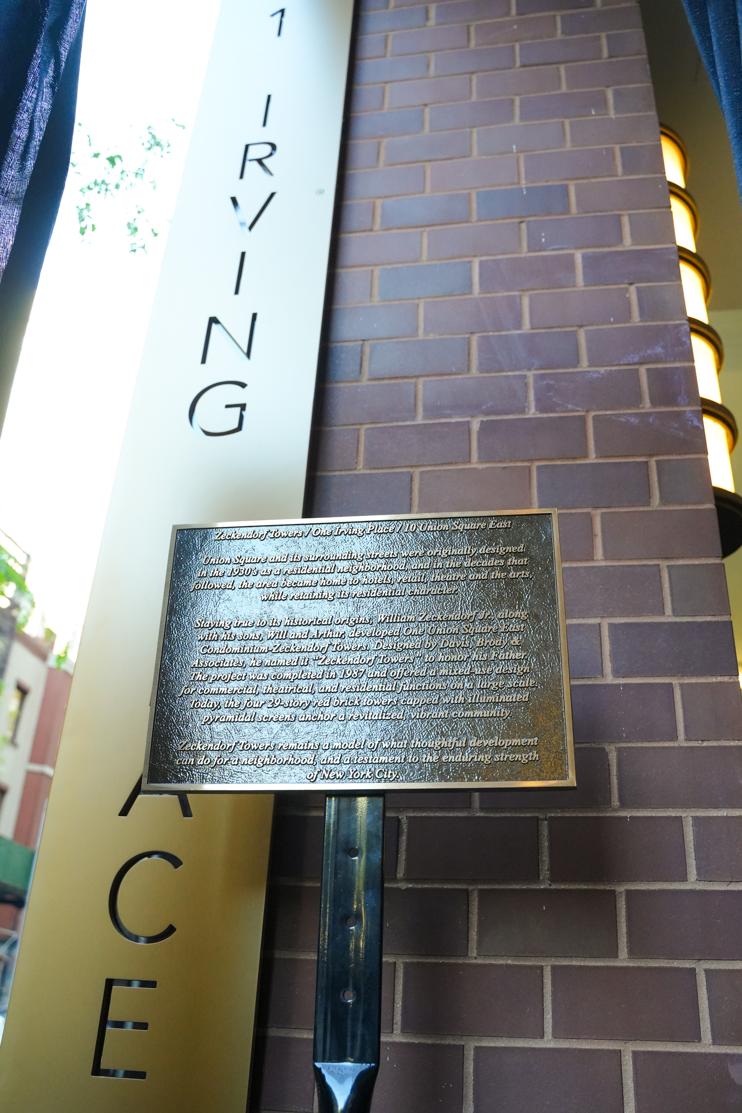 Eine an einem Pfosten befestigte Gedenktafel aus Bronze steht vor einer Backsteinsäule an der Hausnummer 1 Irving Place während einer Enthüllungszeremonie am 11. Oktober 2022 in New York City; darauf sind die Architekturgeschichte und die Entwicklung der Zeckendorf Towers beschrieben. | Quelle: Getty Images