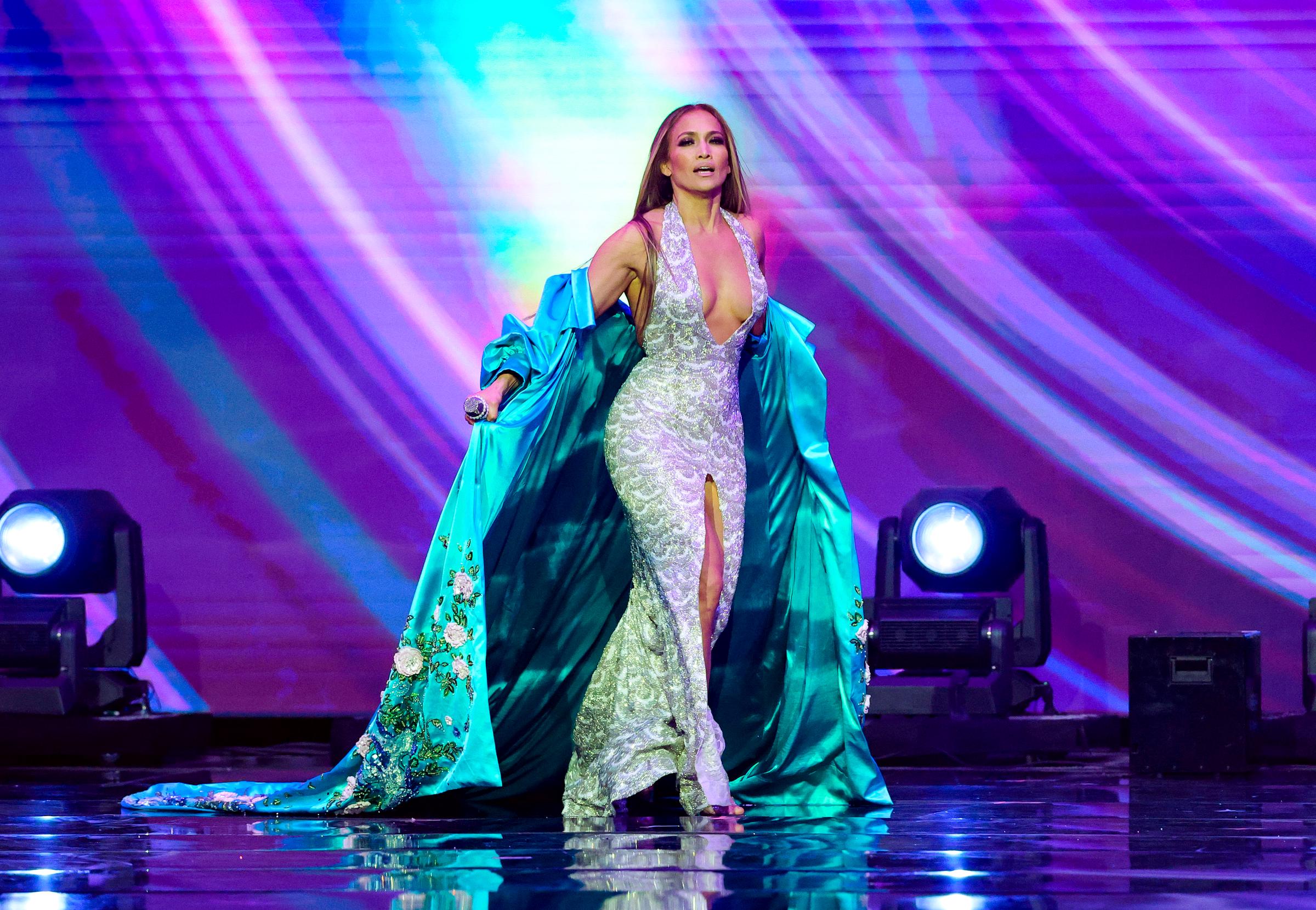 J.Lo schreitet selbstbewusst über die Bühne und hält ihre Robe offen, so dass die Kurven ihres silbernen Kleides im gleißenden Scheinwerferlicht glitzern.
