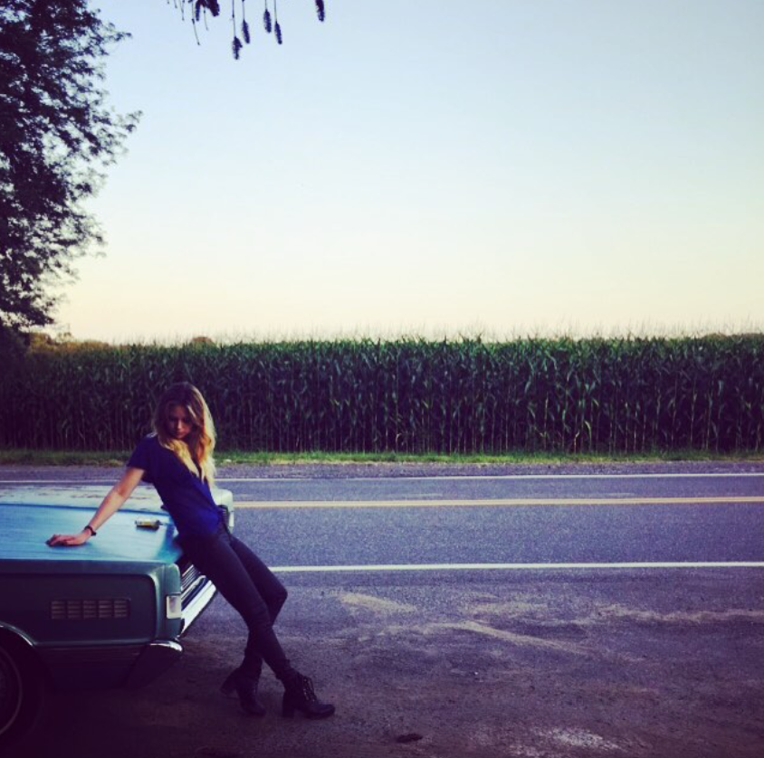 Auf einem Foto, das im August 2015 gepostet wurde – also in den Jahren, bevor sie weitgehend aus der Öffentlichkeit verschwand –, lehnt sich Daveigh Chase an ein geparktes Auto neben einer Landstraße, die von hohen Feldfrüchten gesäumt ist. | Quelle: Instagram/daveighc