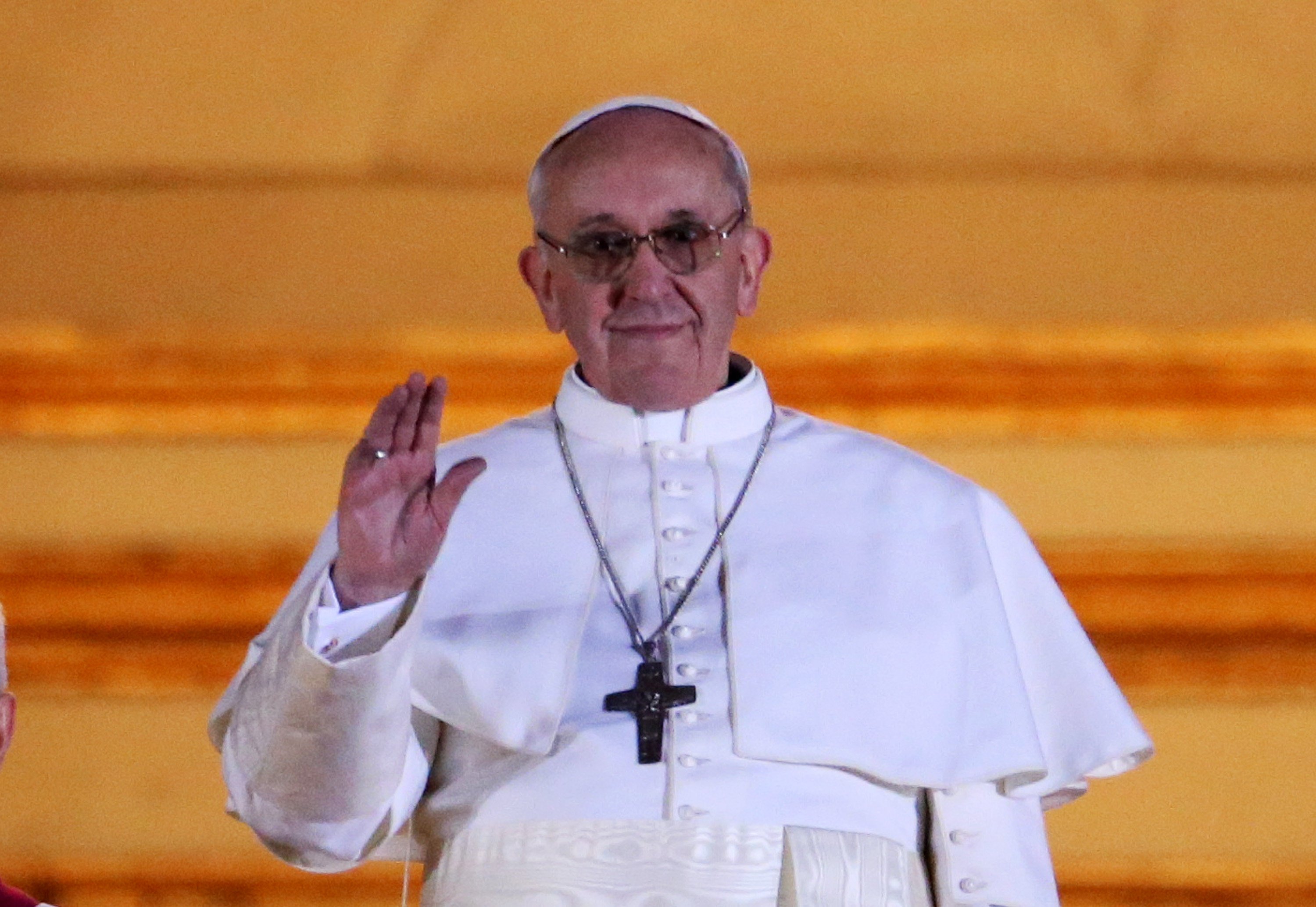 Papst Franziskus grüßt die Menge mit einem sanften Winken, gekleidet in schlichte weiße Gewänder und ein silbernes Kreuz, sein ruhiges Lächeln umrahmt von sanftem goldenen Licht