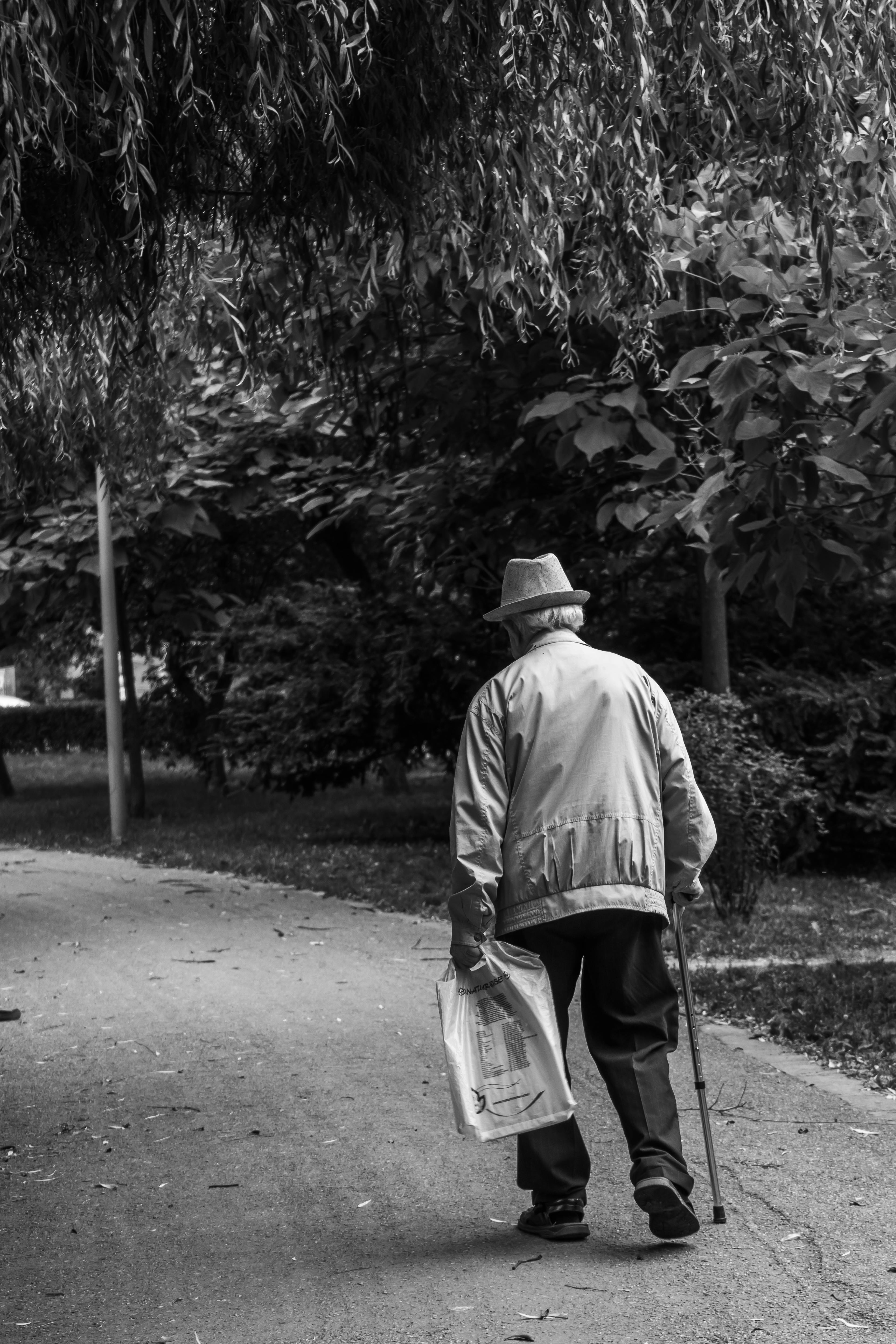 Graustufenbild eines alten Mannes, der mit einem Stock und einer Zeitung geht | Quelle: Pexels