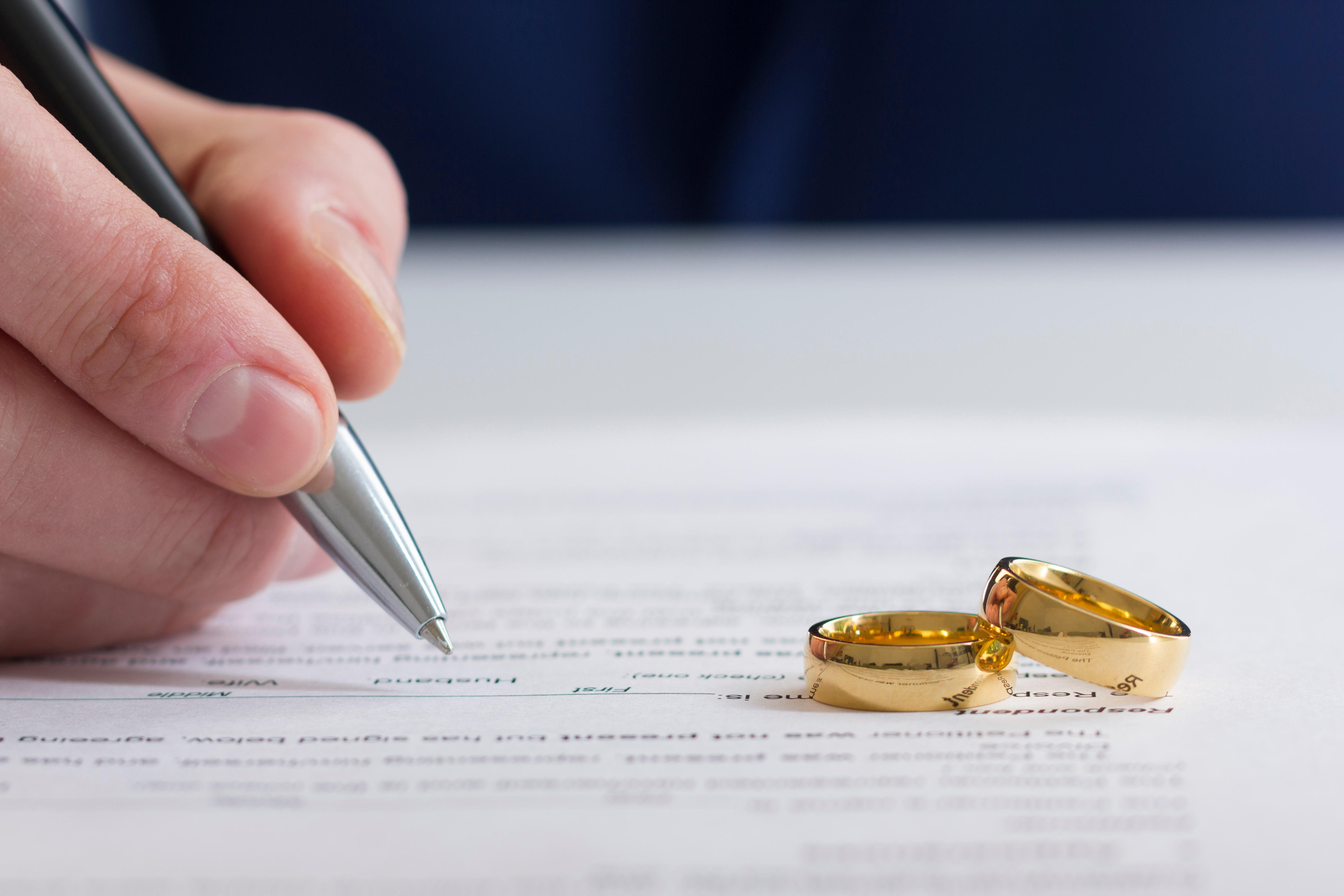 Eine Person, die Scheidungspapiere unterschreibt, während zwei Goldringe in der Nähe liegen | Quelle: Shutterstock