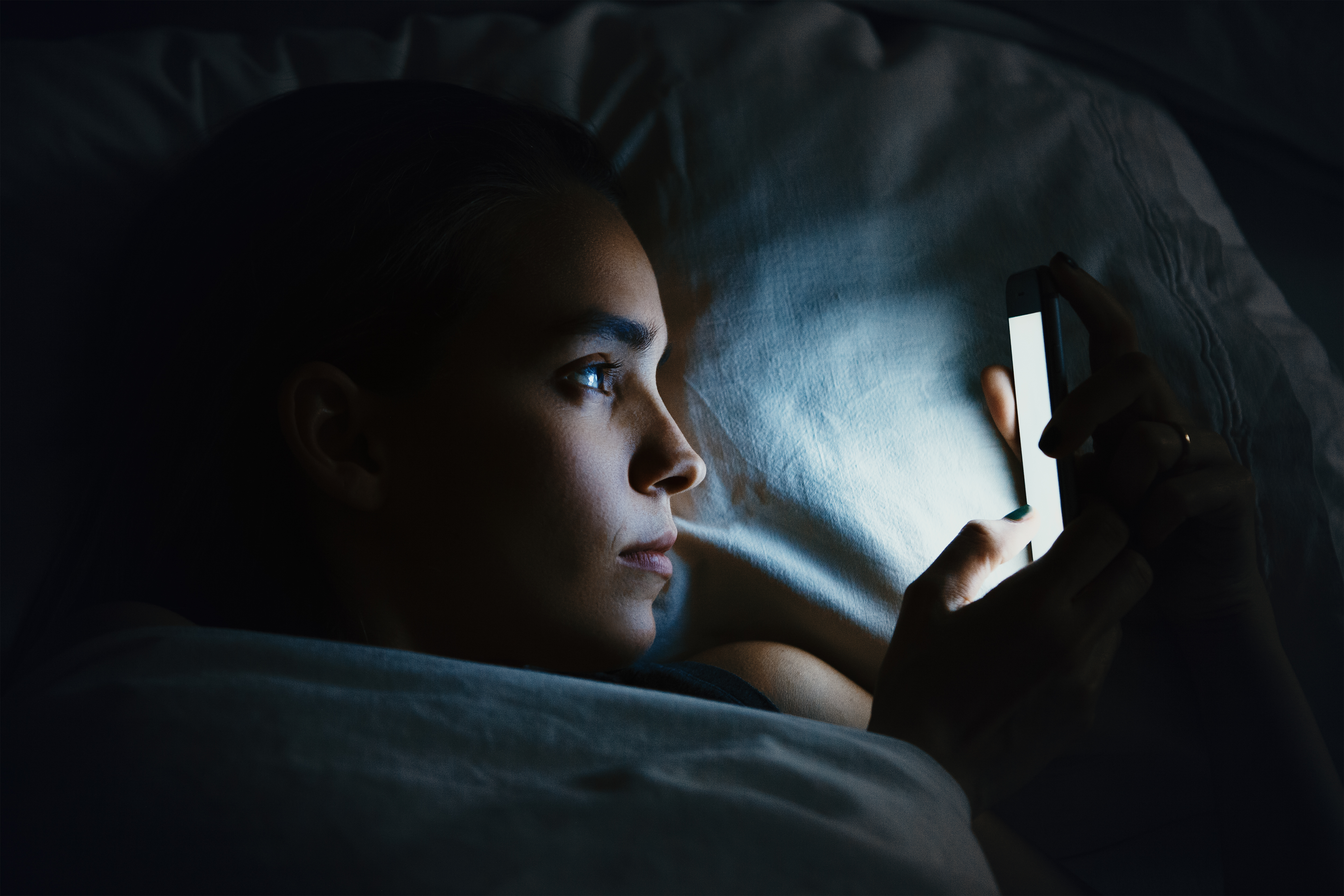 Eine junge Frau benutzt ein Mobiltelefon in einem Bett | Quelle: Shutterstock