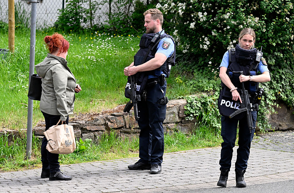 Polizisten informieren einen Anwohner während eines laufenden Banküberfalls, bei dem Verdächtige in Sinzig in Westdeutschland am 8. Mai 2026 mehrere Geiseln genommen haben. | Quelle: Getty Images