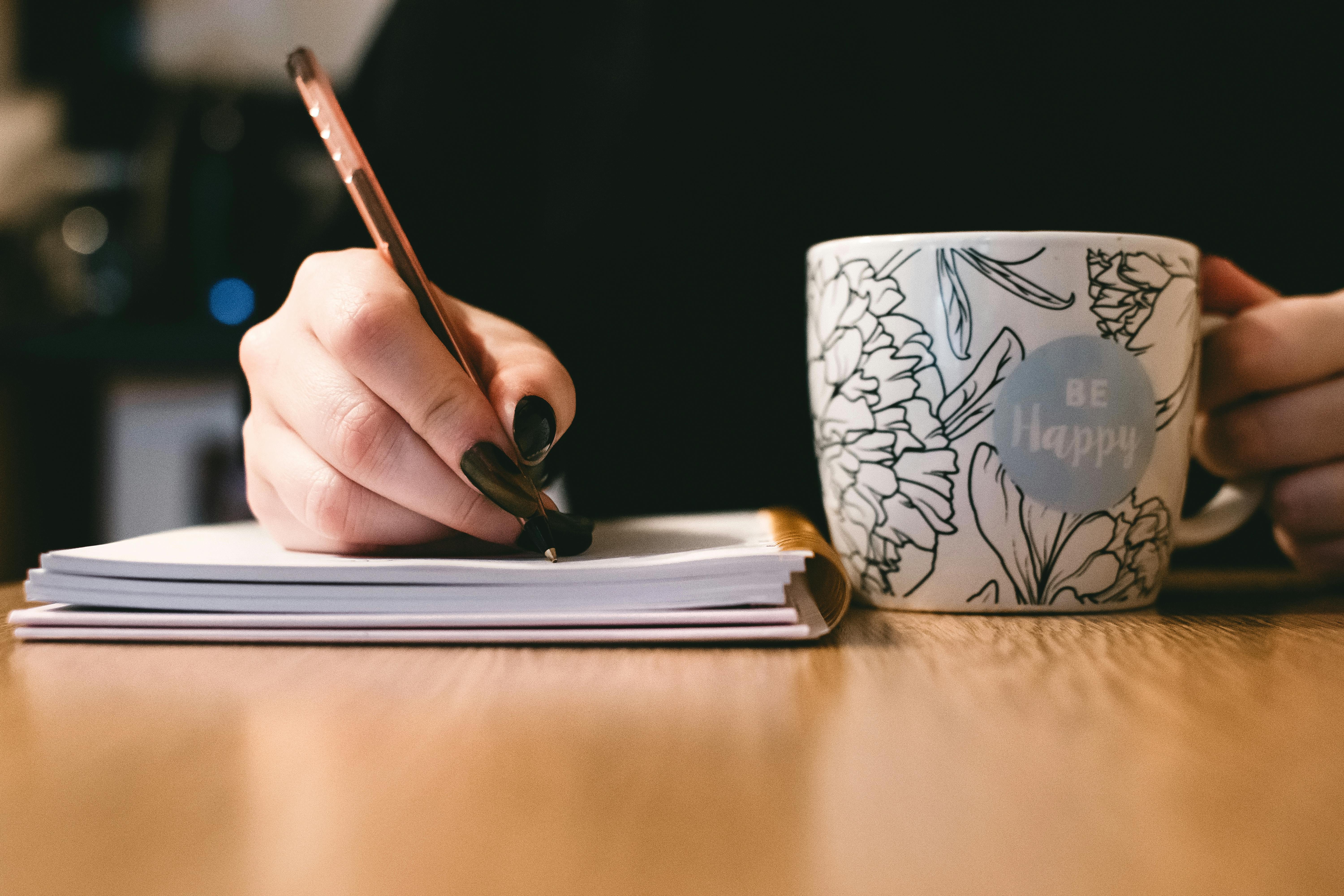 Eine Frau, die mit einer Tasse Kaffee in der Hand auf einen Notizblock schreibt | Quelle: Pexels