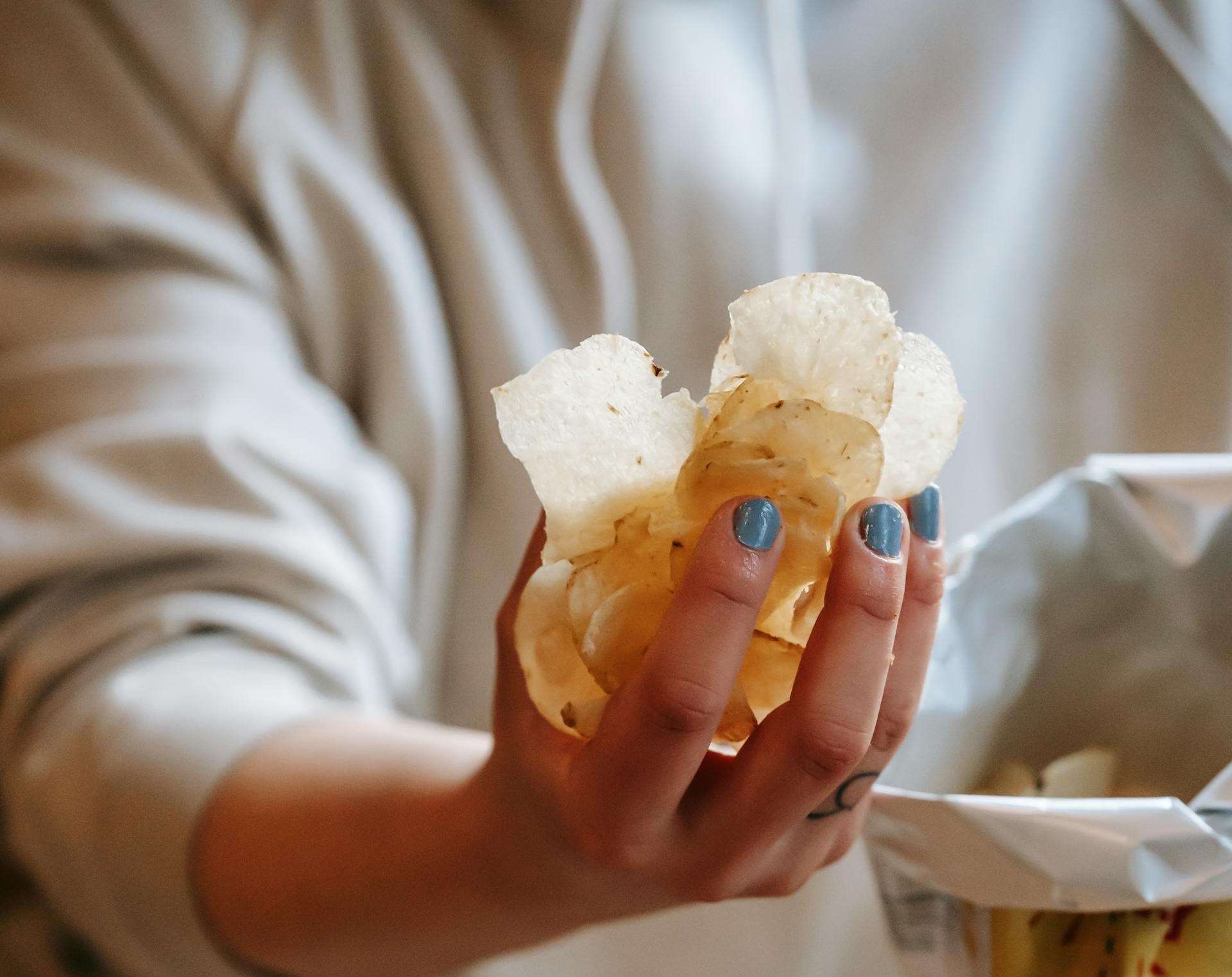Eine Frau hält eine Handvoll Kartoffelchips in der Hand | Quelle: Pexels