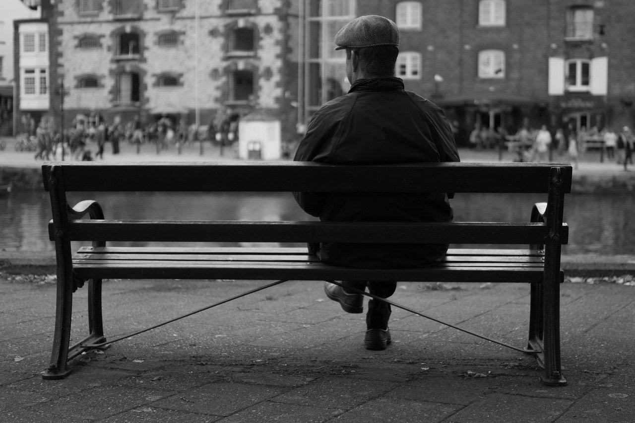 Ein Schwarz-Weiß-Bild eines Mannes, der auf einer Bank sitzt und die Aussicht vor sich betrachtet | Quelle: Pixabay