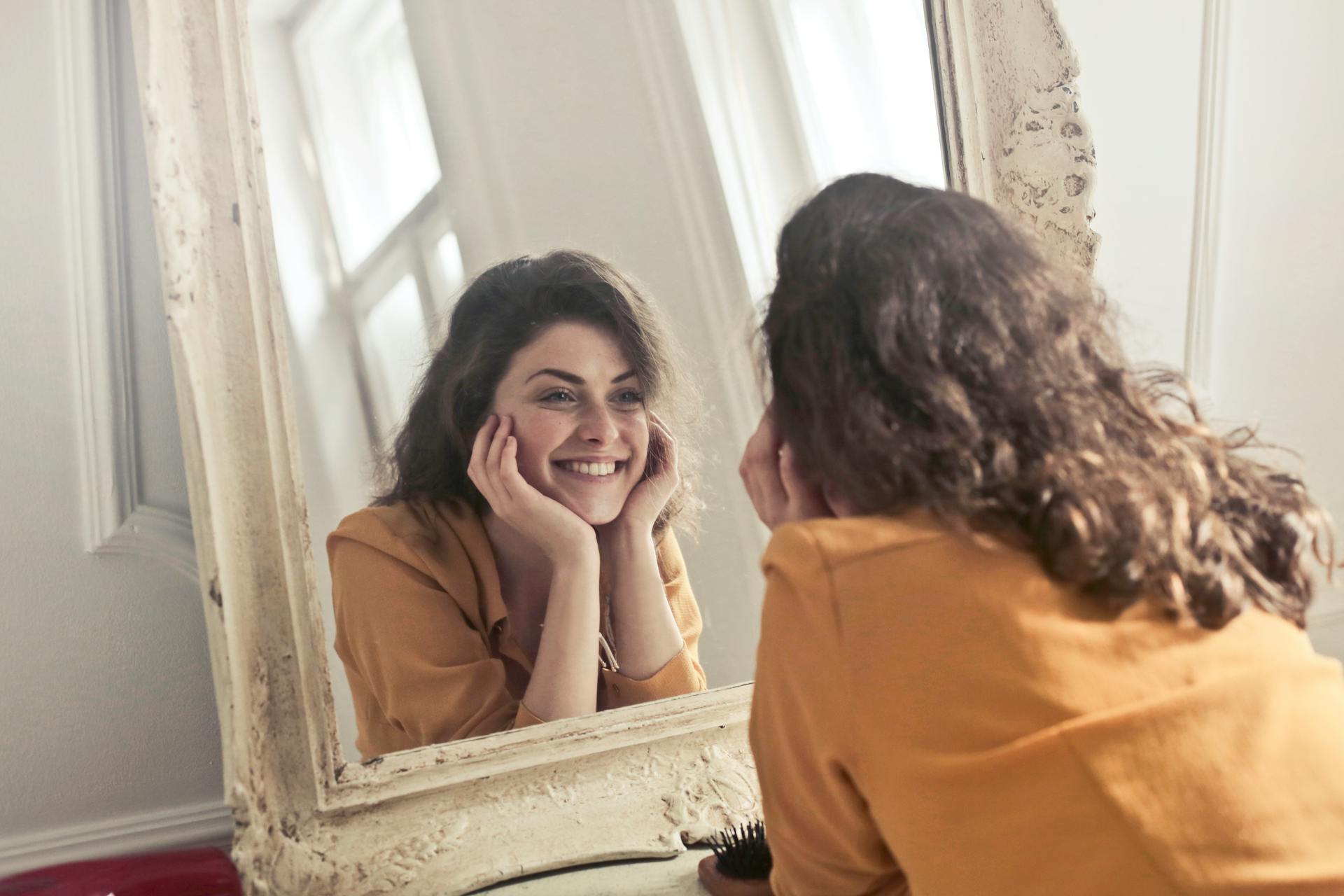 Eine lächelnde Frau, die ihr Spiegelbild betrachtet | Quelle: Pexels