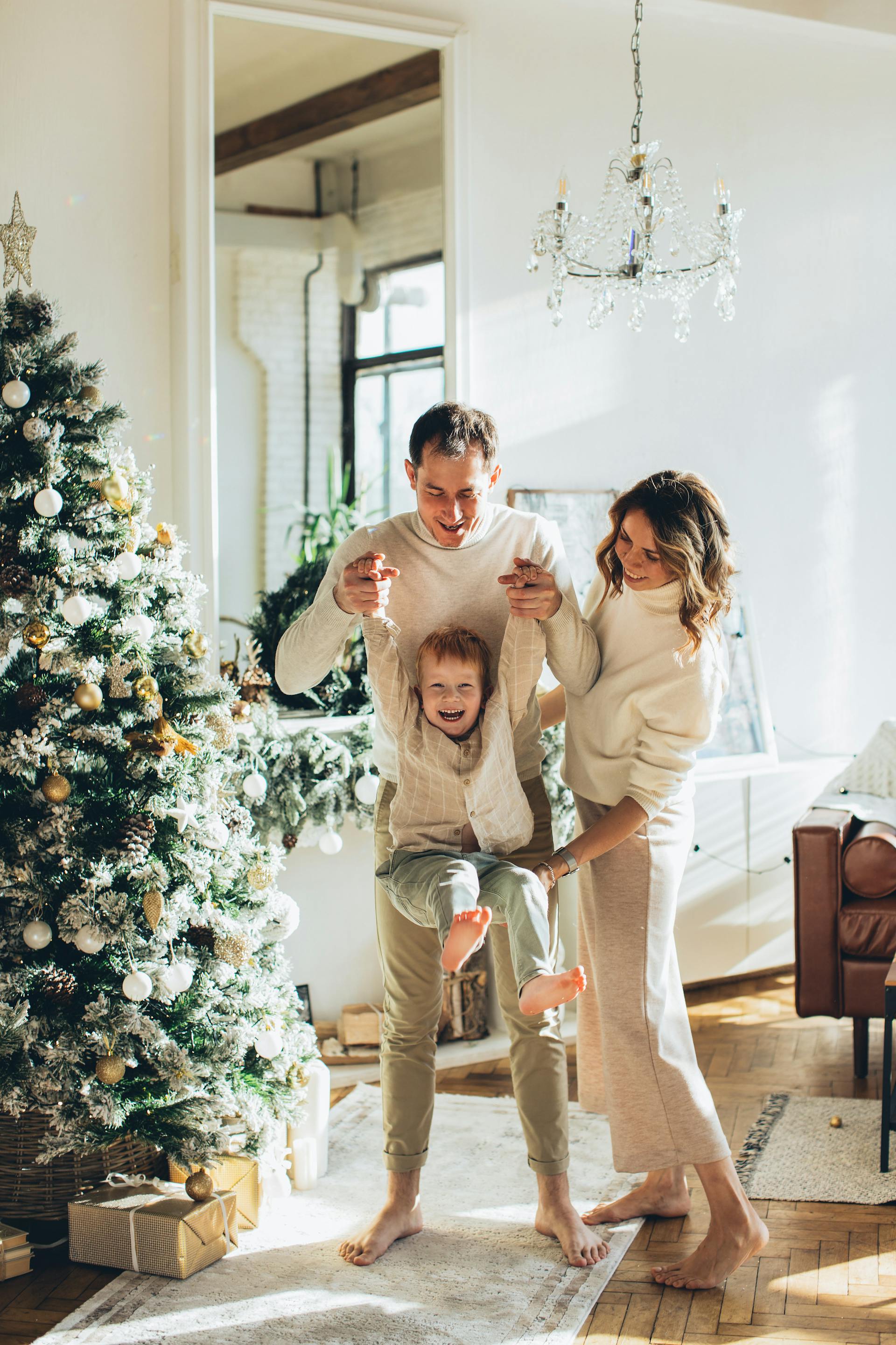 Ein Paar spielt mit seinem kleinen Sohn neben einem Weihnachtsbaum | Quelle: Pexels