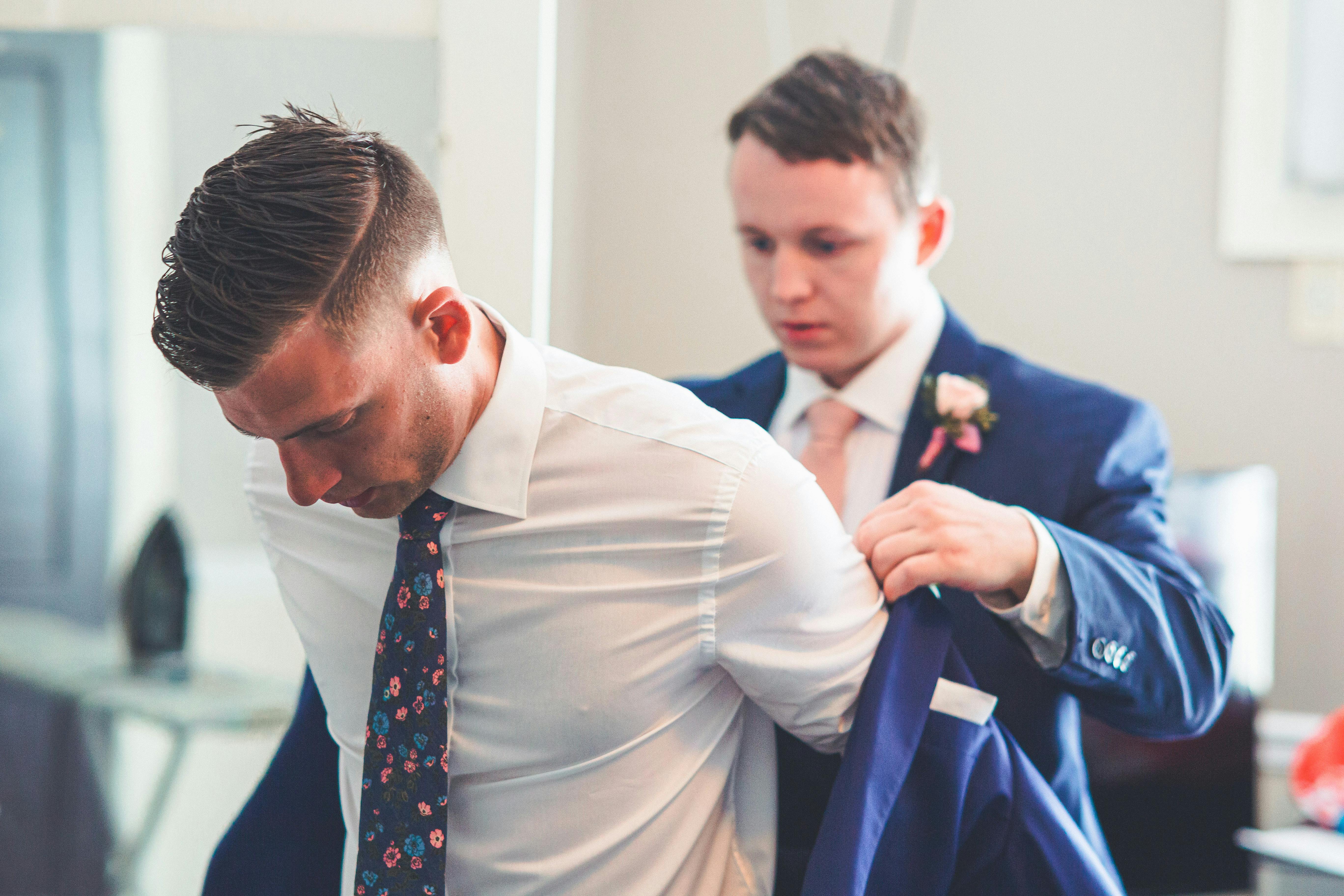 Nur zu Illustrationszwecken. Trauzeuge hilft seinem Bruder beim Anziehen der Anzugsjacke | Quelle: Pexels