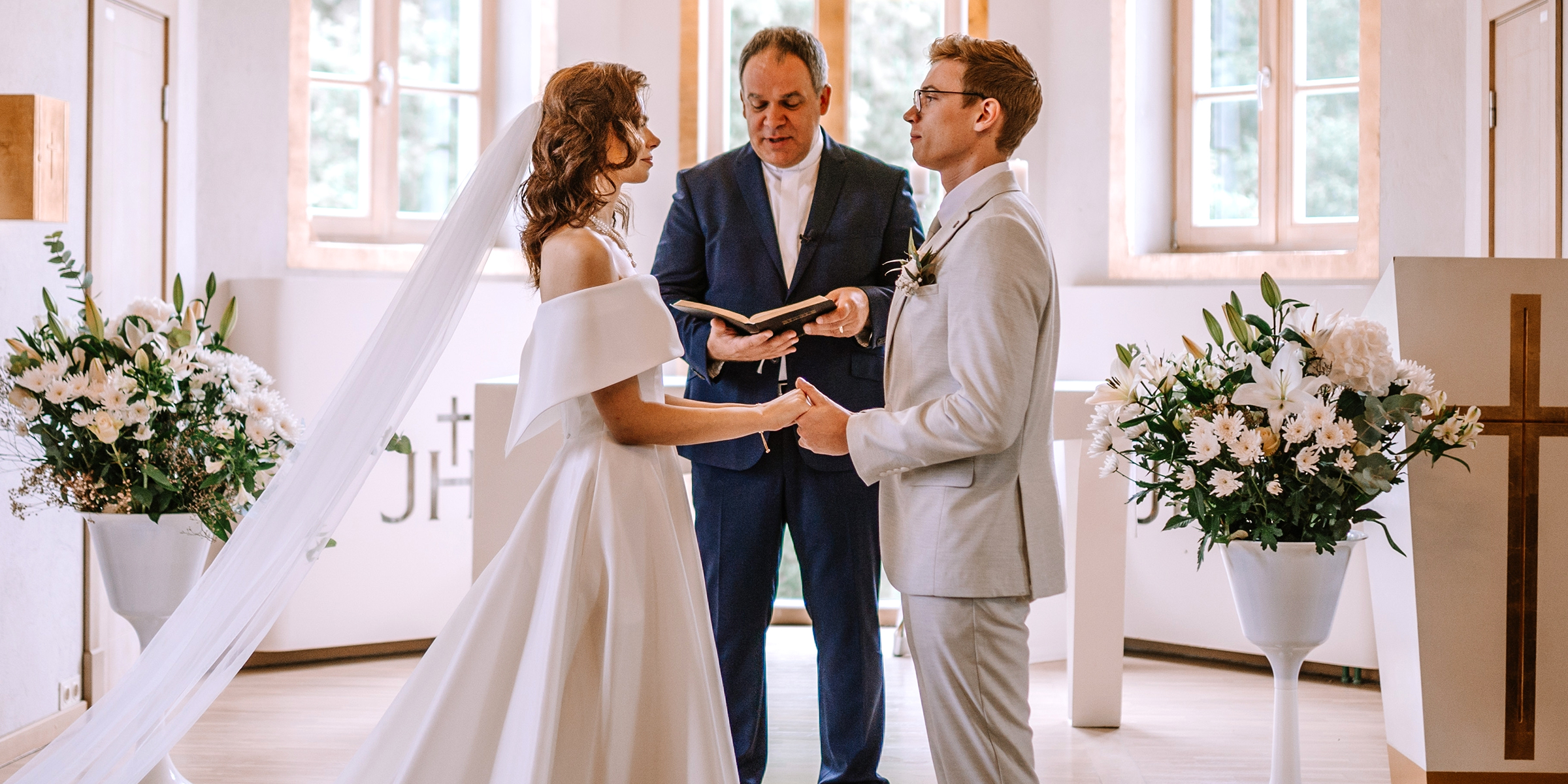 Eine Braut und ein Bräutigam stehen am Altar und halten sich an den Händen, während ein Priester ihr Gelübde verliest | Quelle: Shutterstock