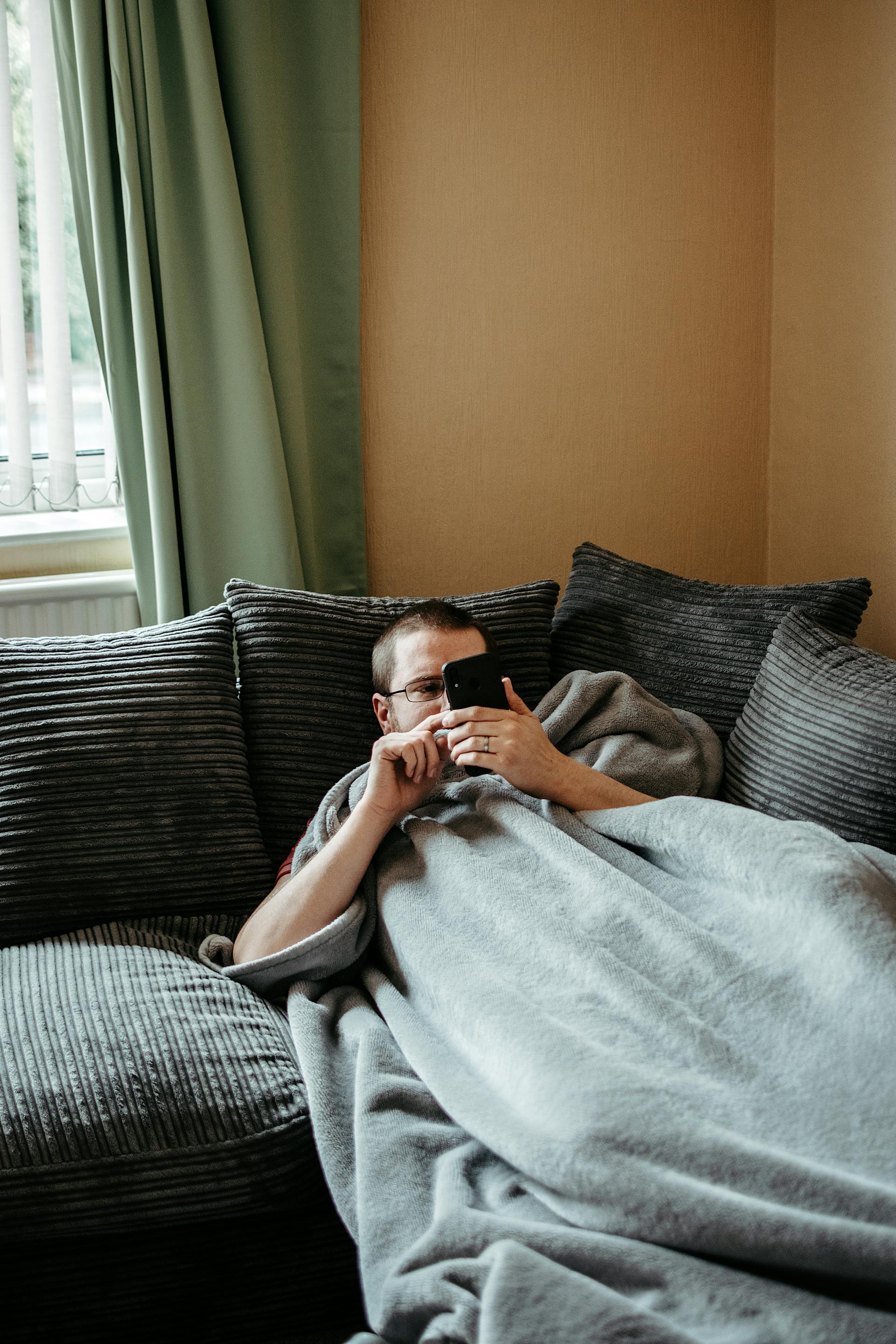 Ein Mann benutzt sein Telefon, während er auf der Couch liegt | Quelle: Pexels