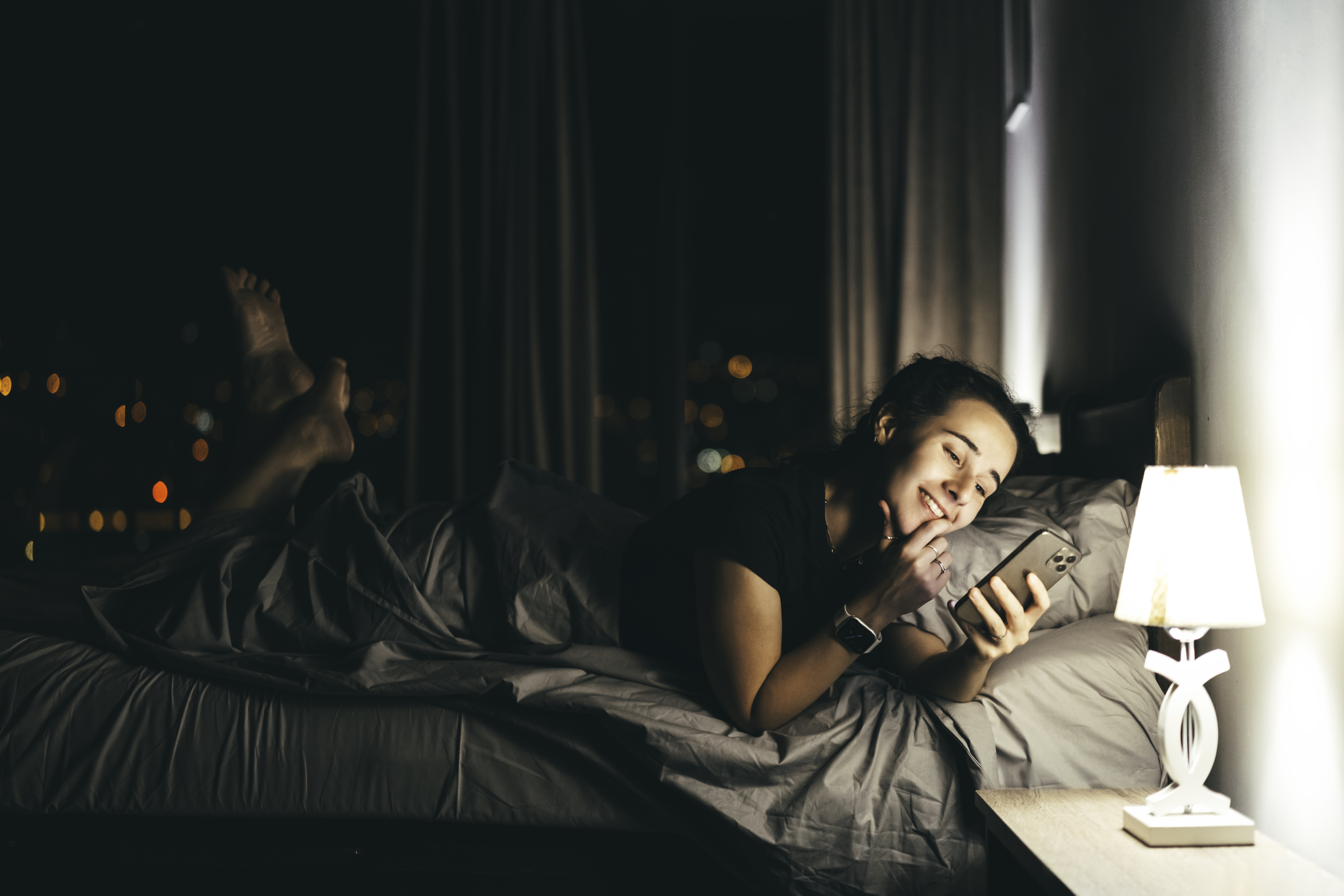 Glückliche Person, die im Bett liegt und ihr Telefon hält | Quelle: Getty Images
