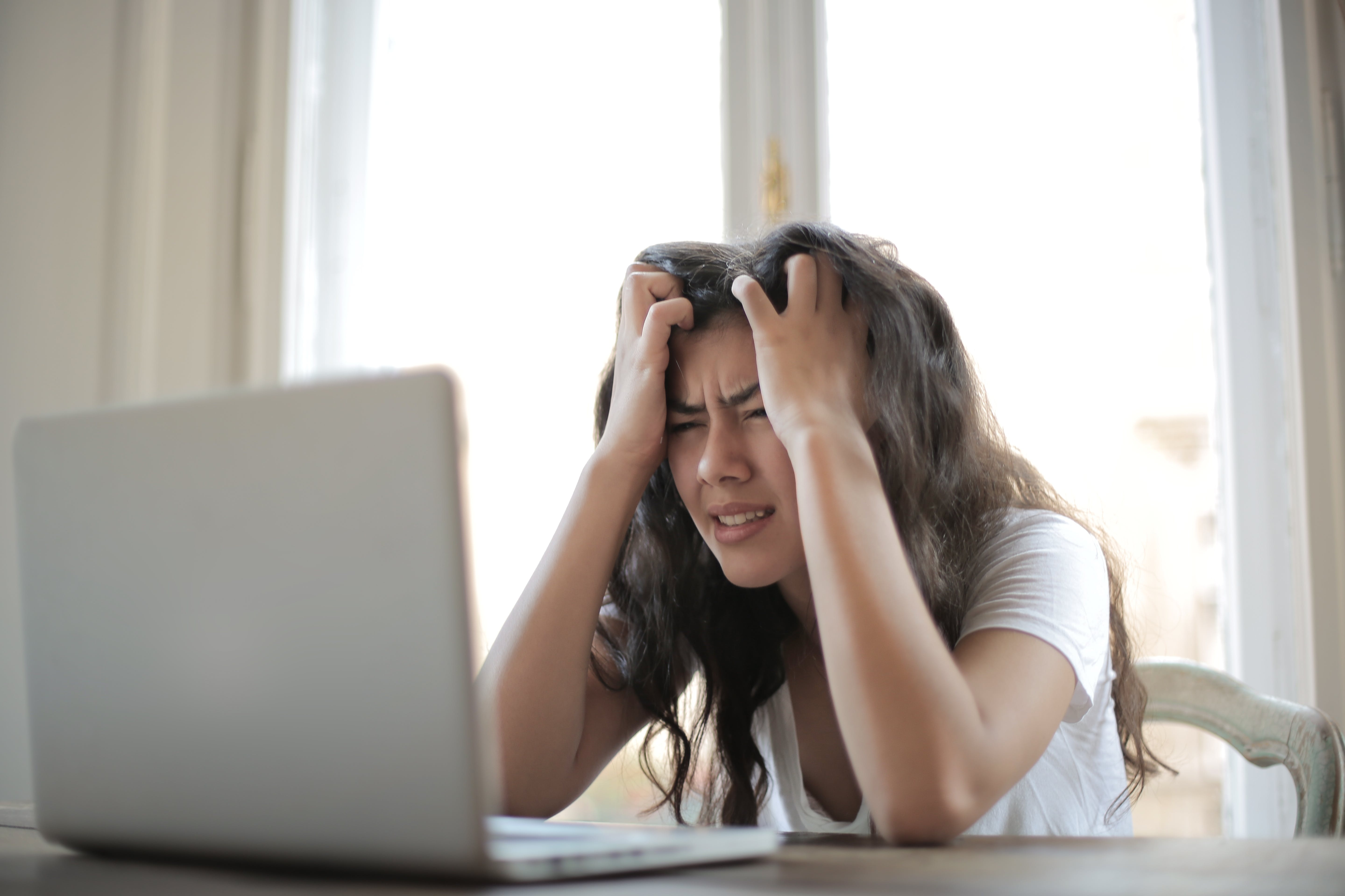 Eine frustrierte Frau fährt sich mit den Händen durch die Haare, während sie auf einen Laptop schaut | Quelle: Pexels